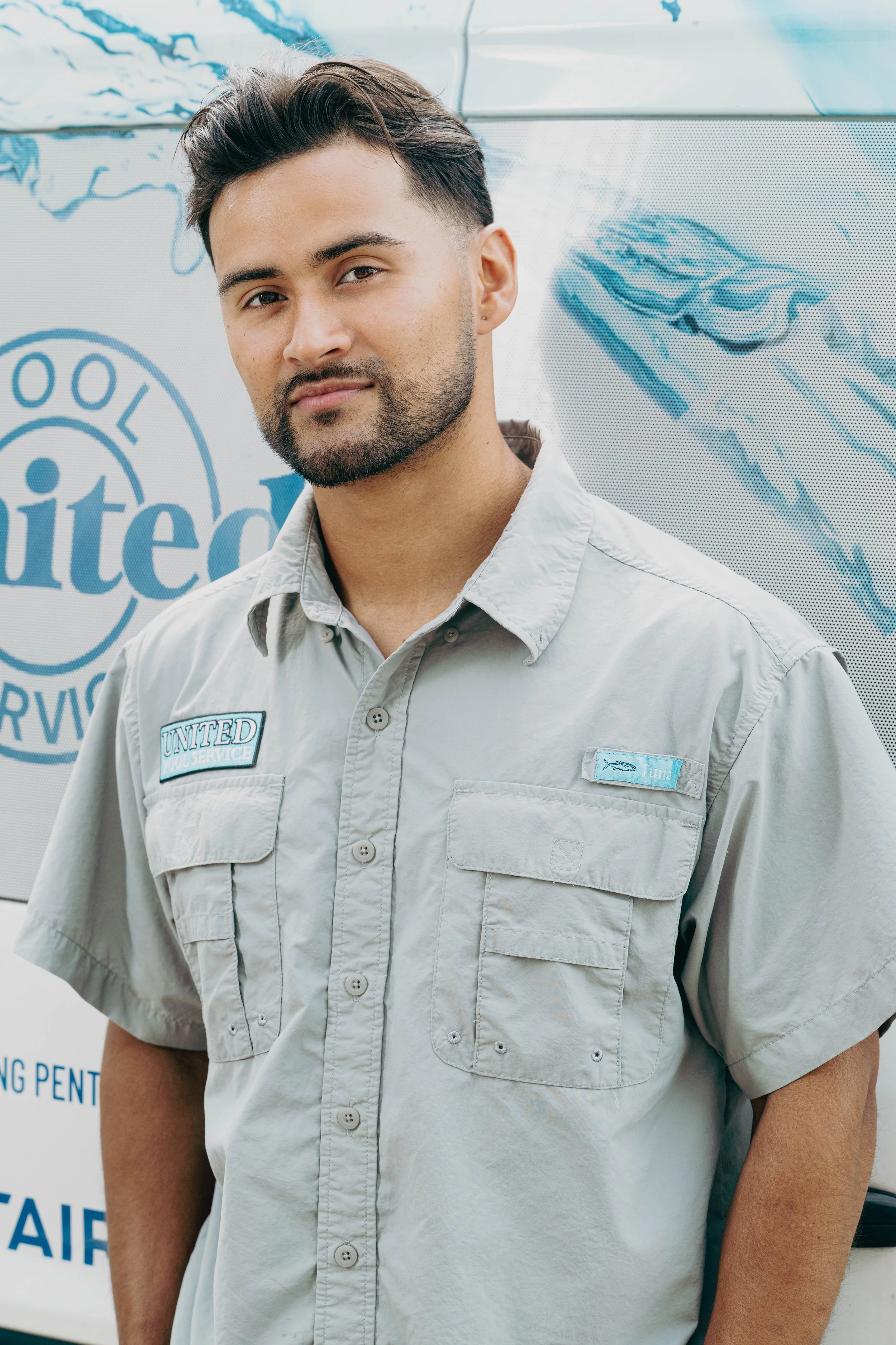 A man in uniform standing in front of a vehicle with 'United' and 'Pool Service' logos, wearing a light gray shirt with 'United' patches.
