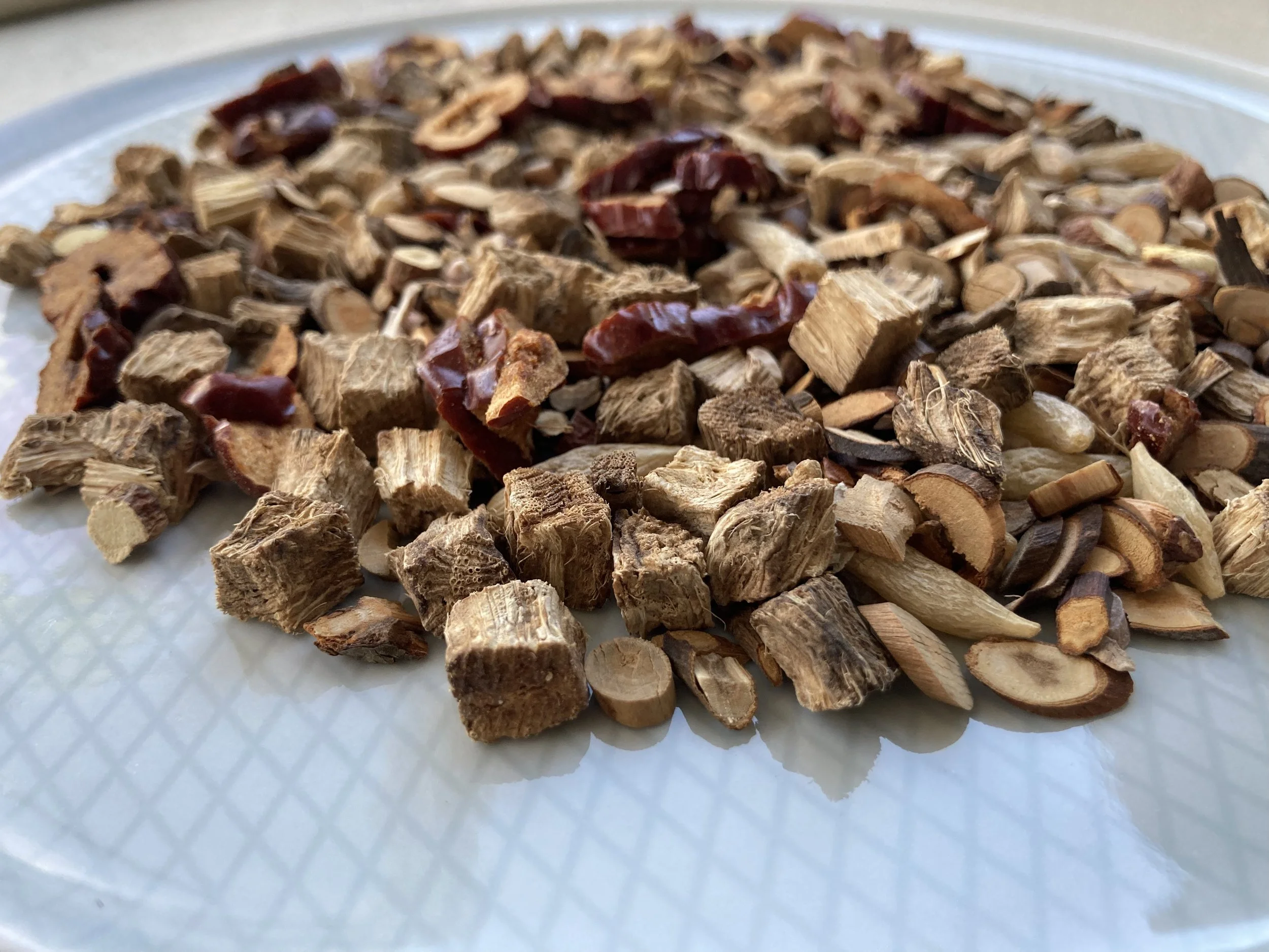 An assortment of dried Chinese herbs, different shades of brown, white and dark red, piled on a blue plate.