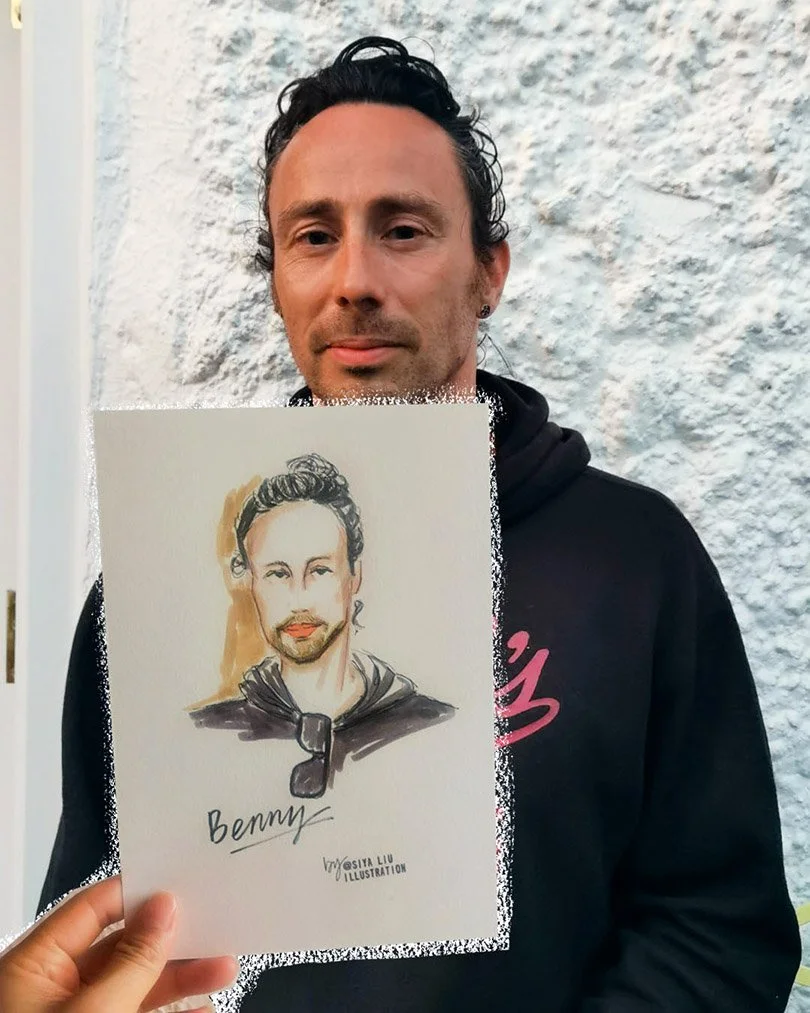 A man with dark hair holds up a quick portrait by Siya Liu at a private event. 