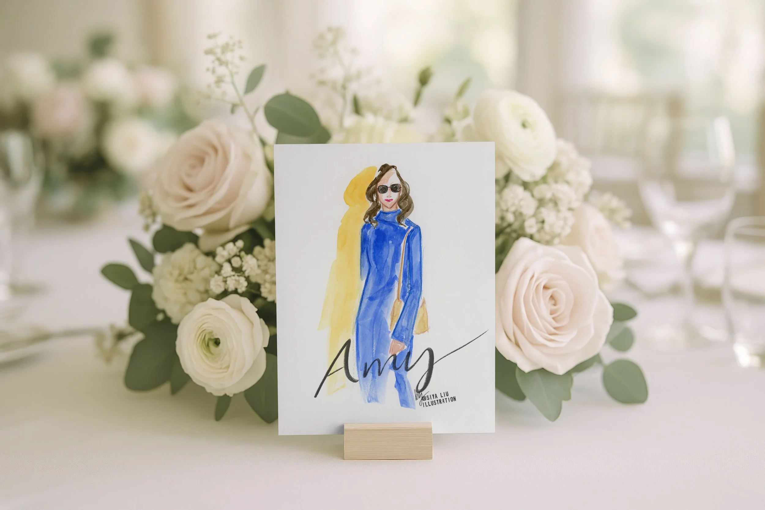 A fashion illustration of a lady named Amy, dressed in a blue dress and wearing sunglasses, as a luxury event or wedding place card and keepsake gift, hand-illustrated by Siya Liu, Live Event Artist at a live event.