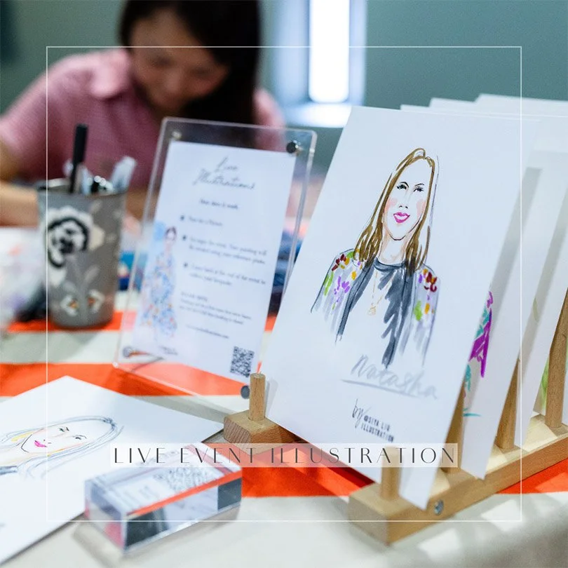 A photo of Siya Liu drawing at a live illustration station with a personalised fashion portrait of a long-haired lady in a dark floral outfit. 