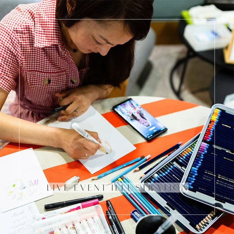 A photo of Siya Liu drawing at a live illustration station with a photo as a reference. 