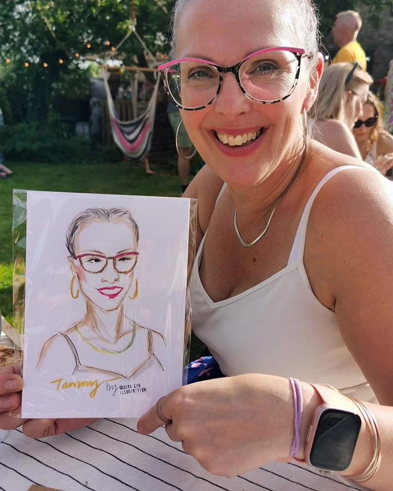 A lady in funky pink glasses holds up a quick portrait by Siya Liu at a private event. 