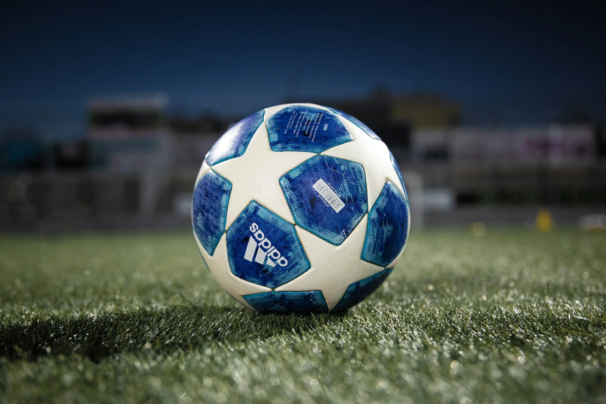 Soccer ball with Adidas branding on a grassy field at night.
