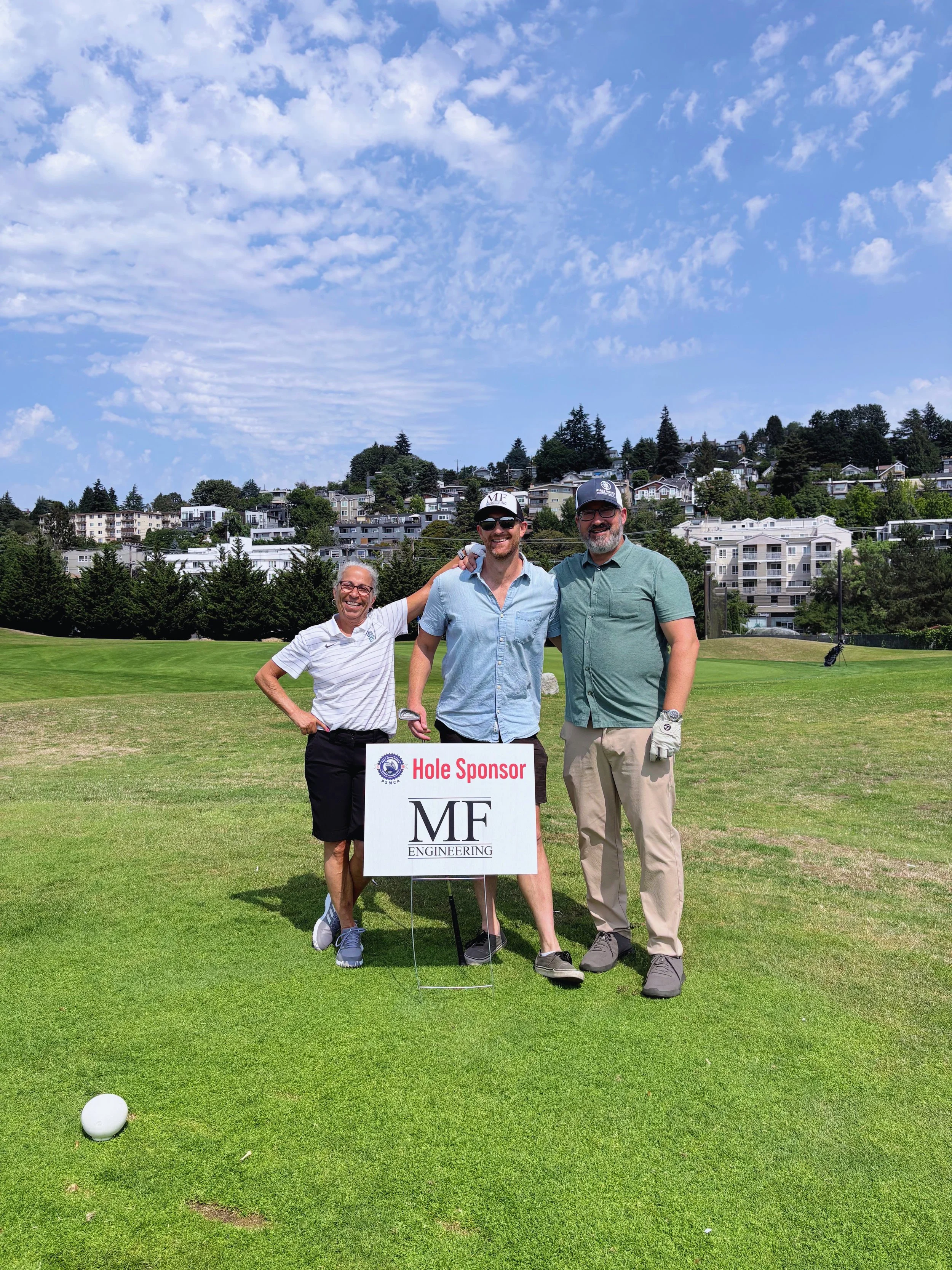 Sue Goheen, Kale Stephenson and Kuhrt Wieneke pose by MF Engineering's hole sponsor sign.