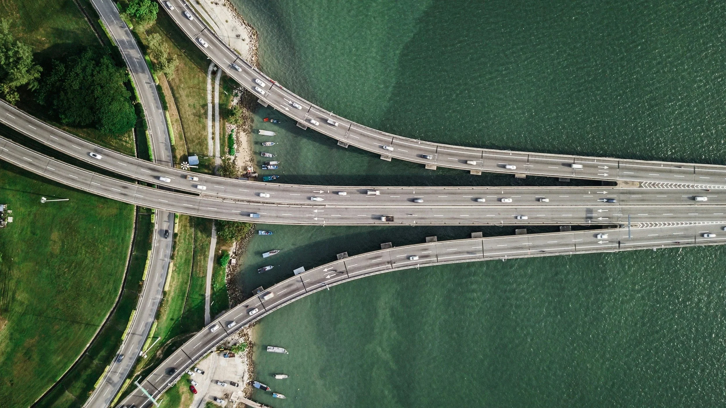 Aerial view of multiple bridges crossing over a body of water with boats docked underneath and green parks on the sides.