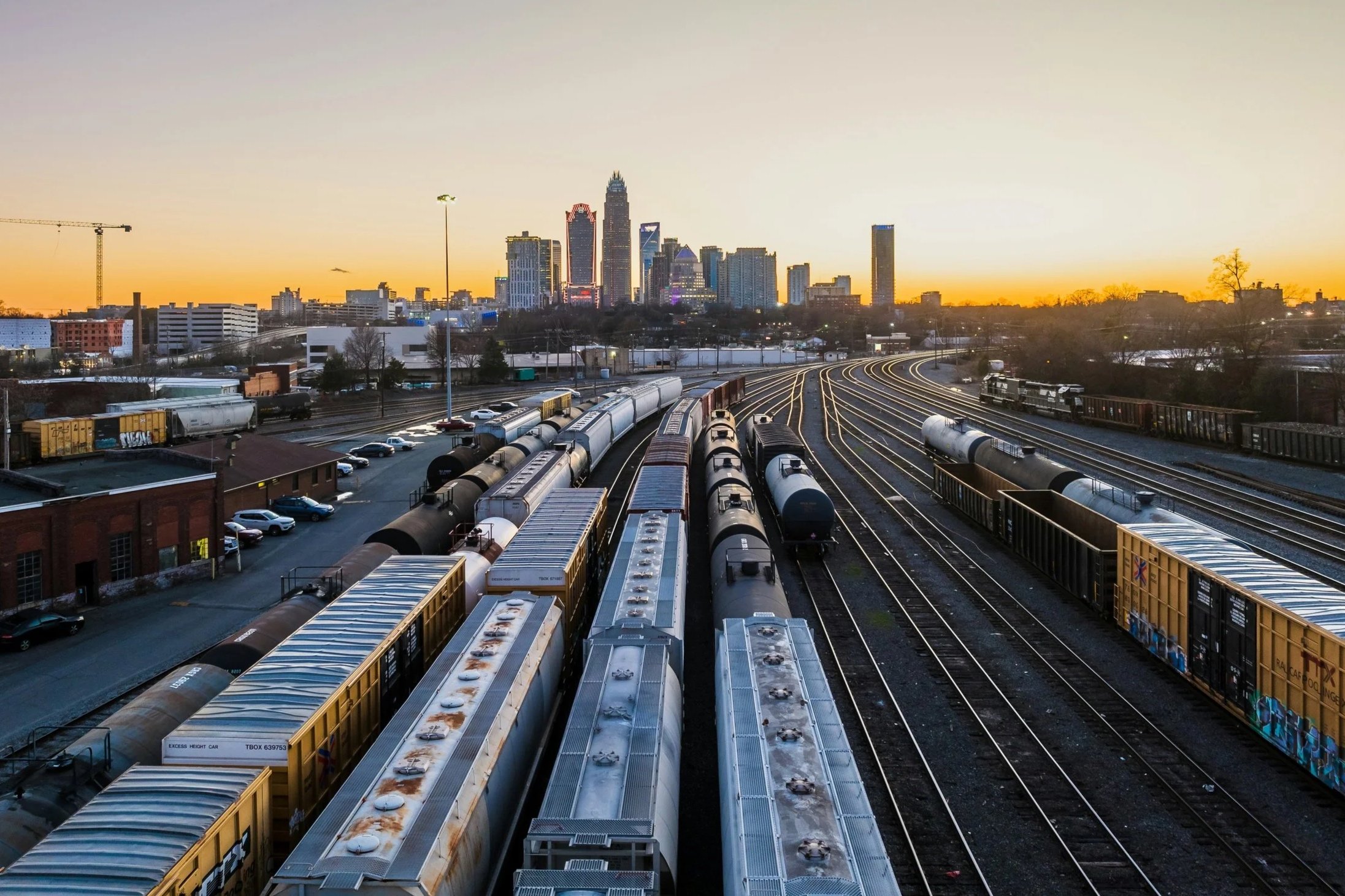 Multiple train cars on railroad tracks during sunset with a city skyline in the background.