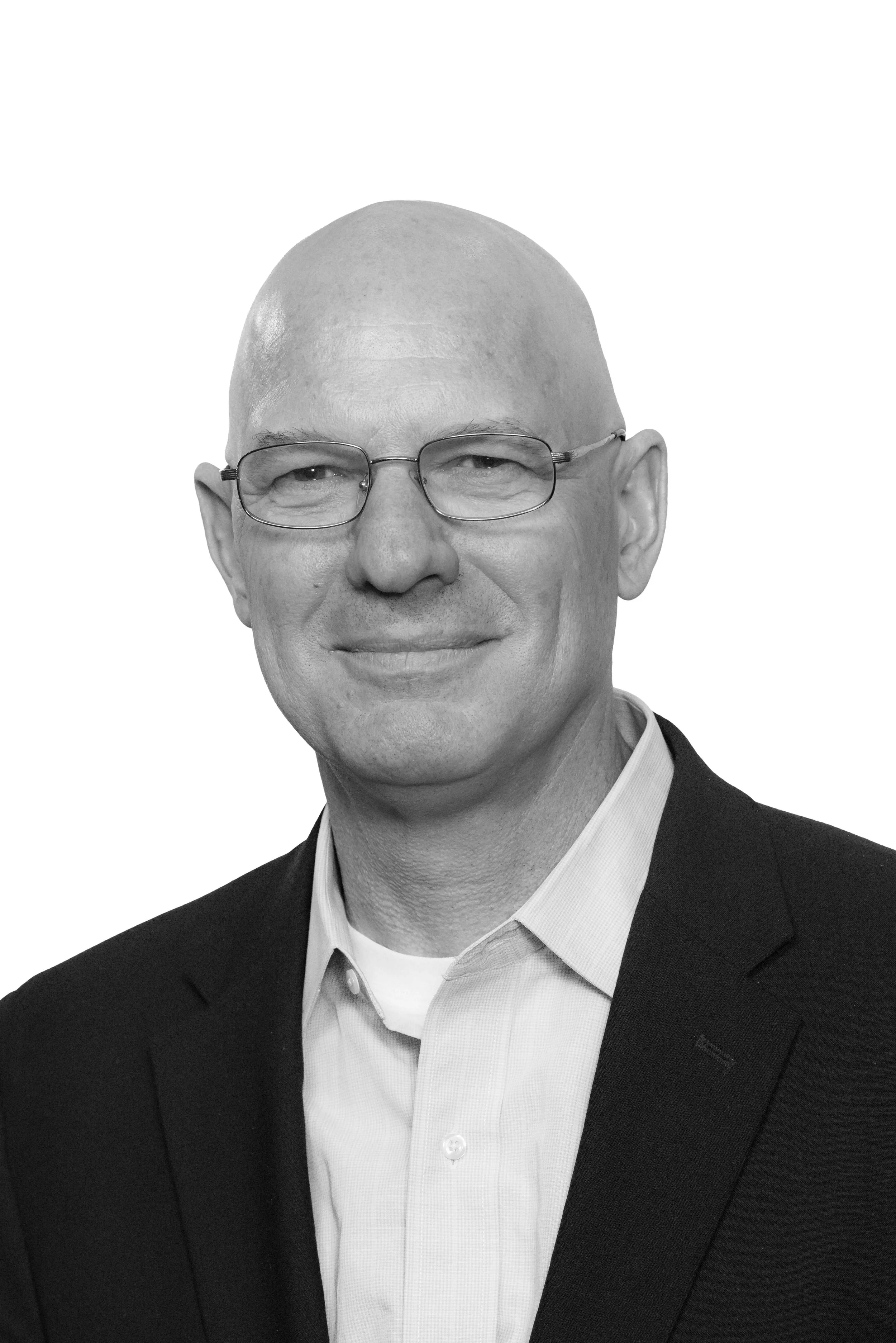Black-and-white portrait of a bald man wearing glasses, a white collared shirt, and a dark blazer, smiling slightly.