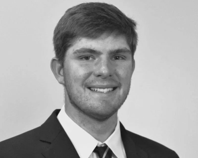 Black and white photo of a young man wearing a suit and tie, smiling at the camera.
