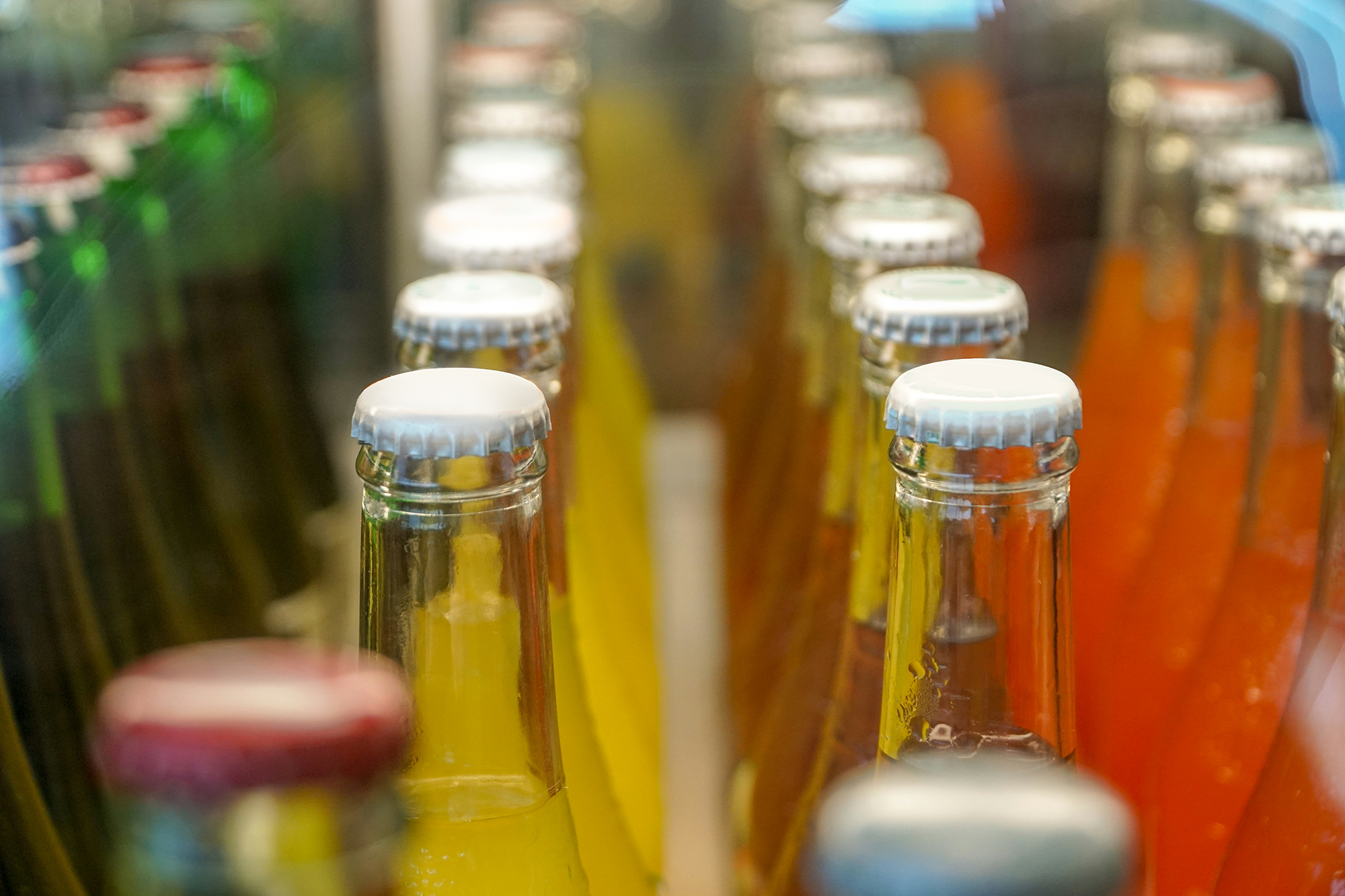 Close-up of glass bottles with colorful drinks on a store shelf, capped with white bottle caps.