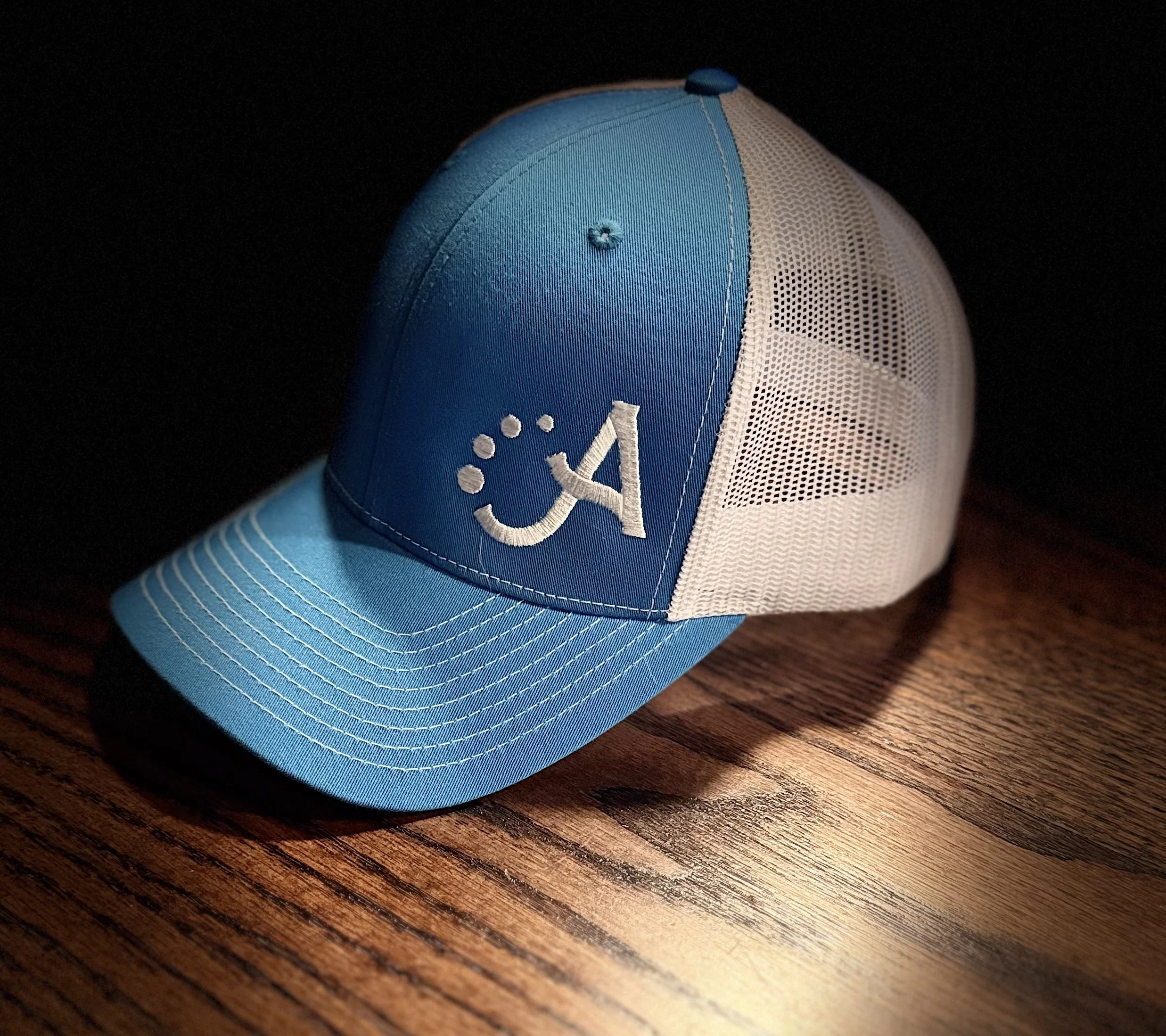 A blue and white mesh baseball cap with an embroidered logo and a curved brim, resting on a wooden surface.