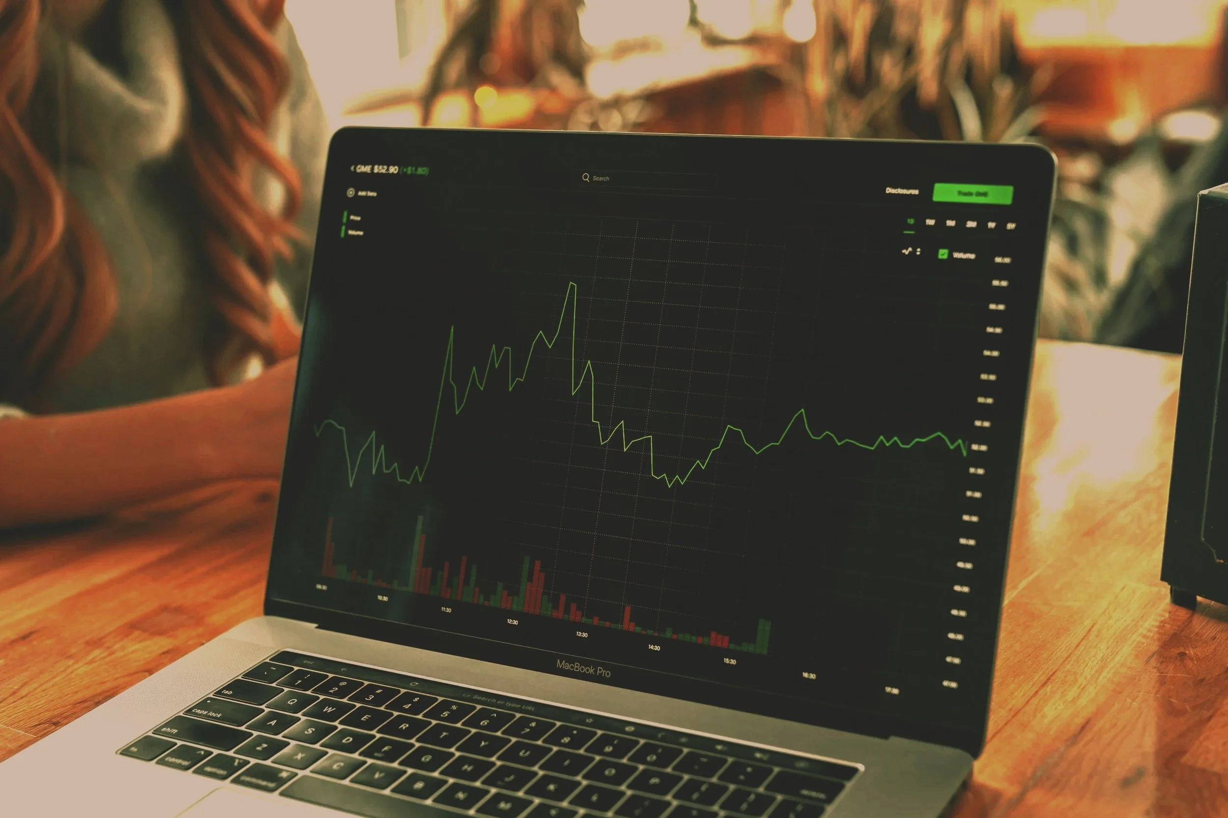 Laptop on wooden table displaying a financial stock chart in a cozy indoor setting.