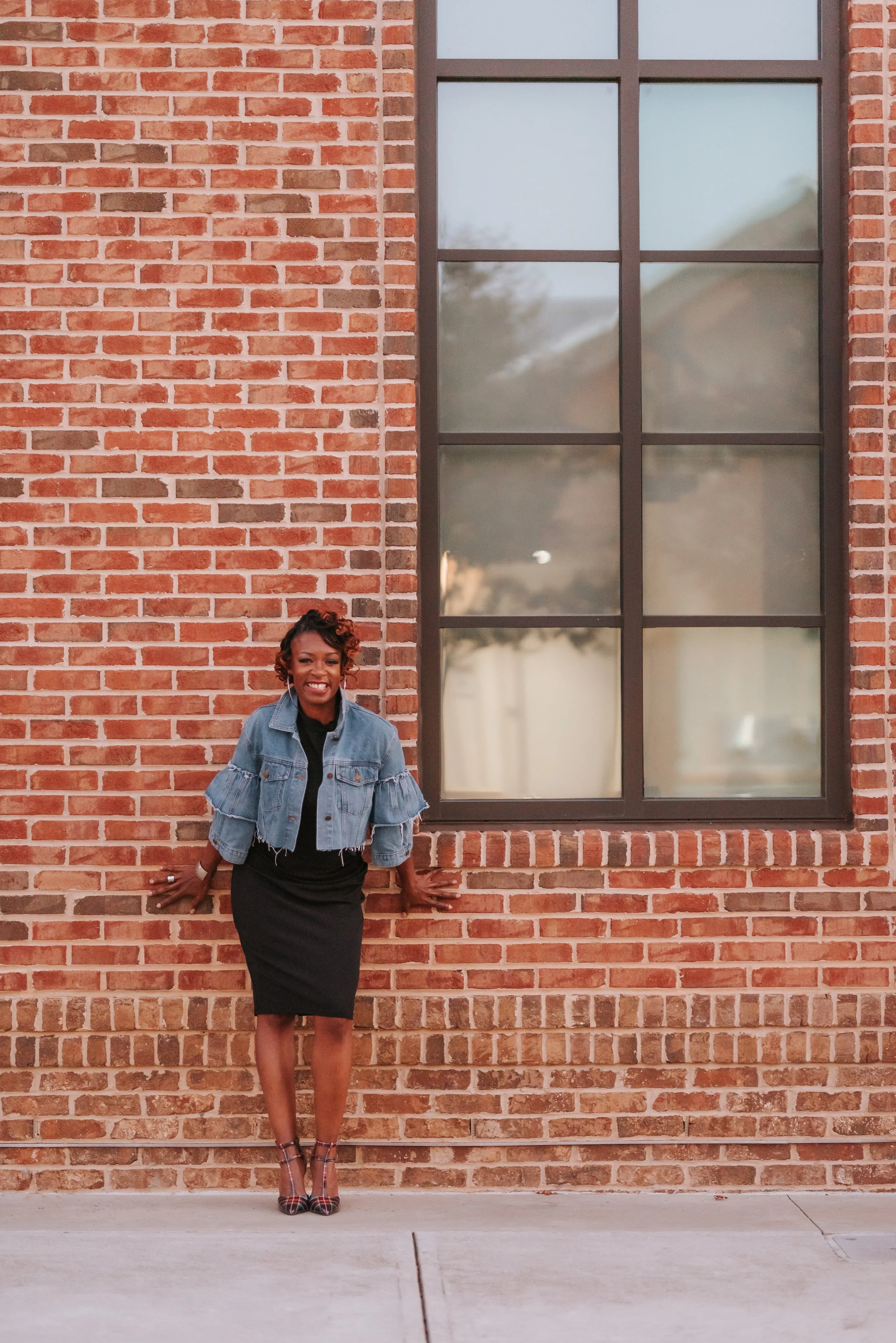 Sonia smiling leaning against a brick wall