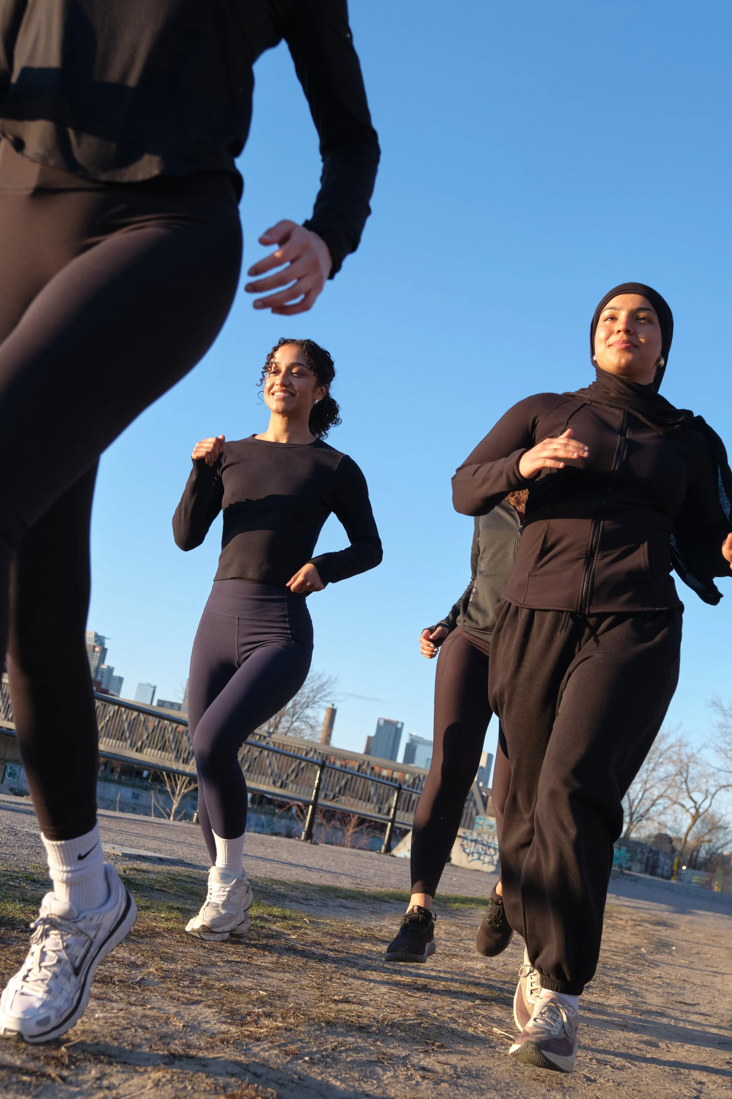 Group of people jogging or running outdoors during daytime, with city skyline in background.