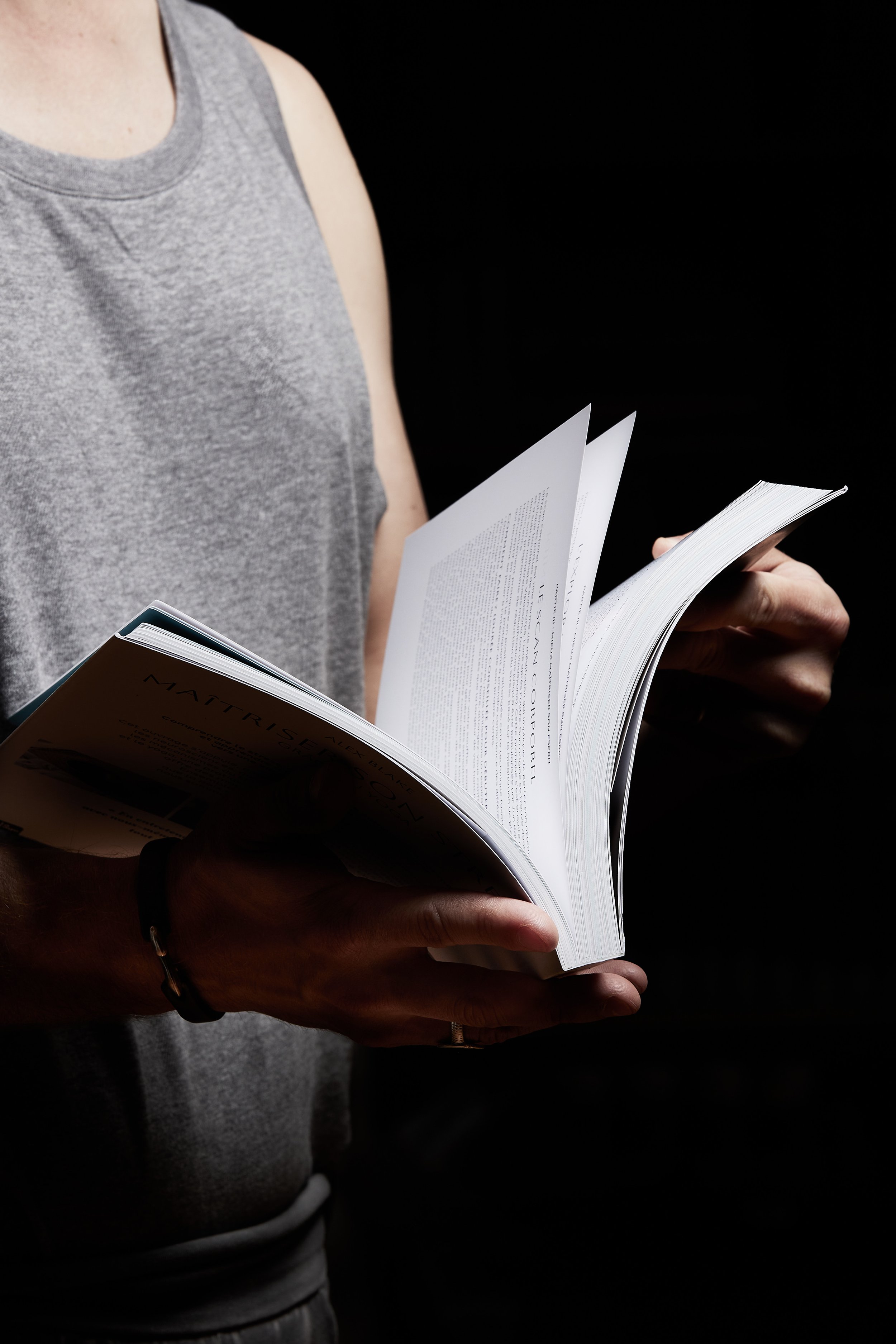 Personne en t-shirt gris tenant un livre ouvert, fond noir. Alex Blake Yoga