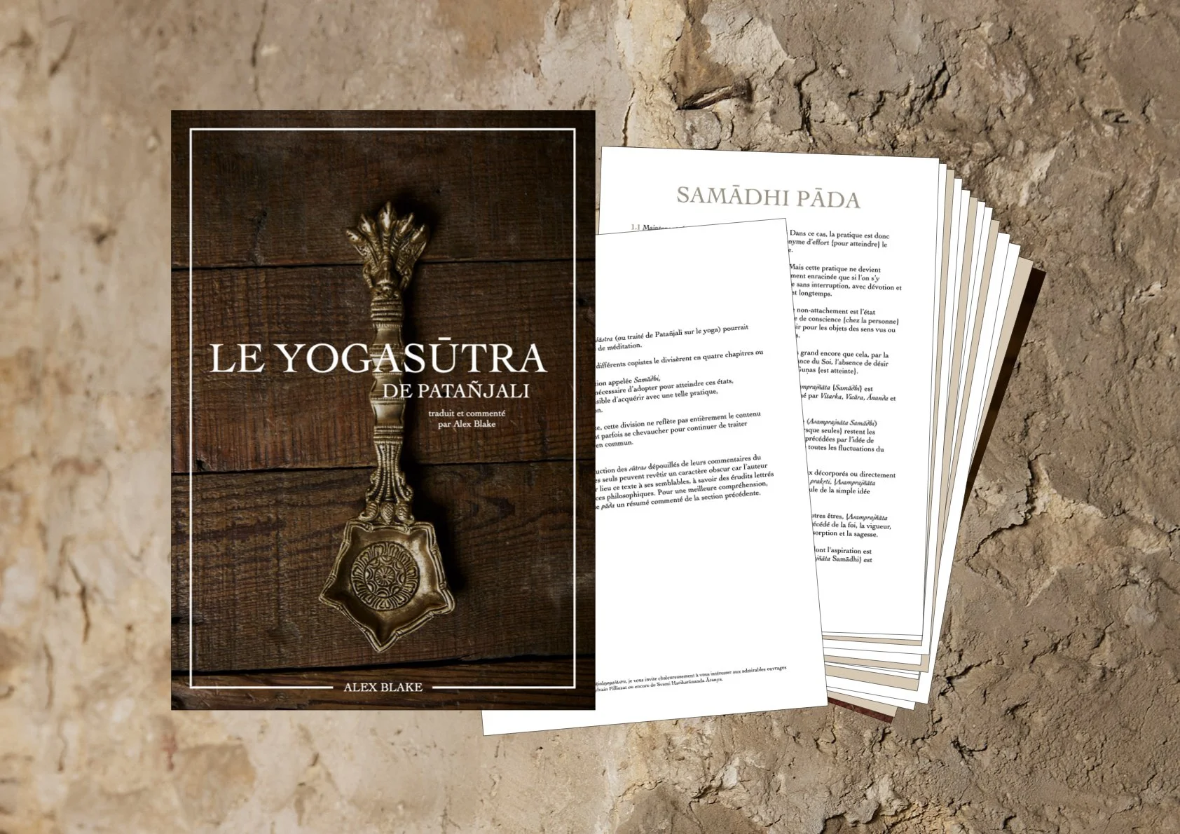 Une brochure intitulée "Le Yogasûtra de Patañjali" avec une image d'une antique louche en bronze sur une surface en bois, et plusieurs pages de notes ou d'articles empilées à côté, posée sur une surface rocheuse.