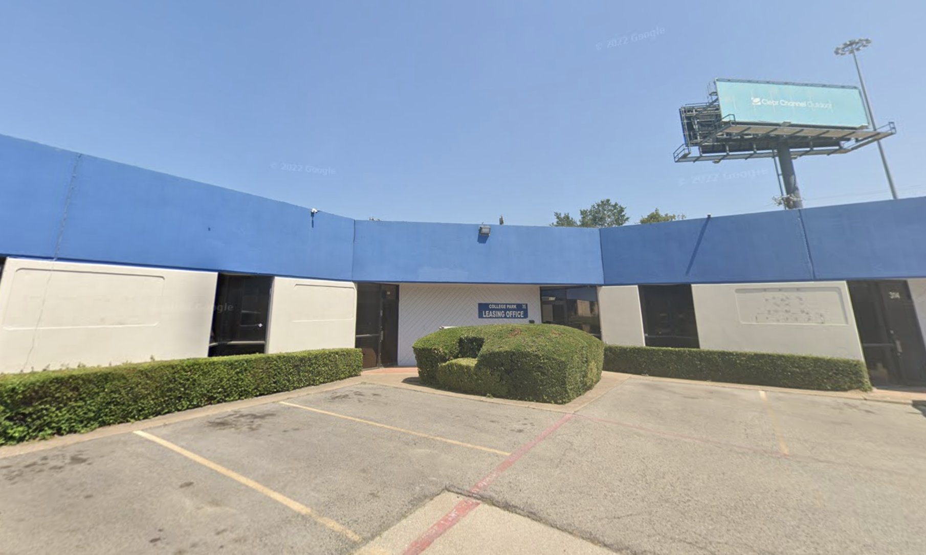 Exterior of a building with a blue upper section, beige lower section, and a sign that reads 'College Park Leasing Office' above the entrance, with landscaping and parking spaces in front.
