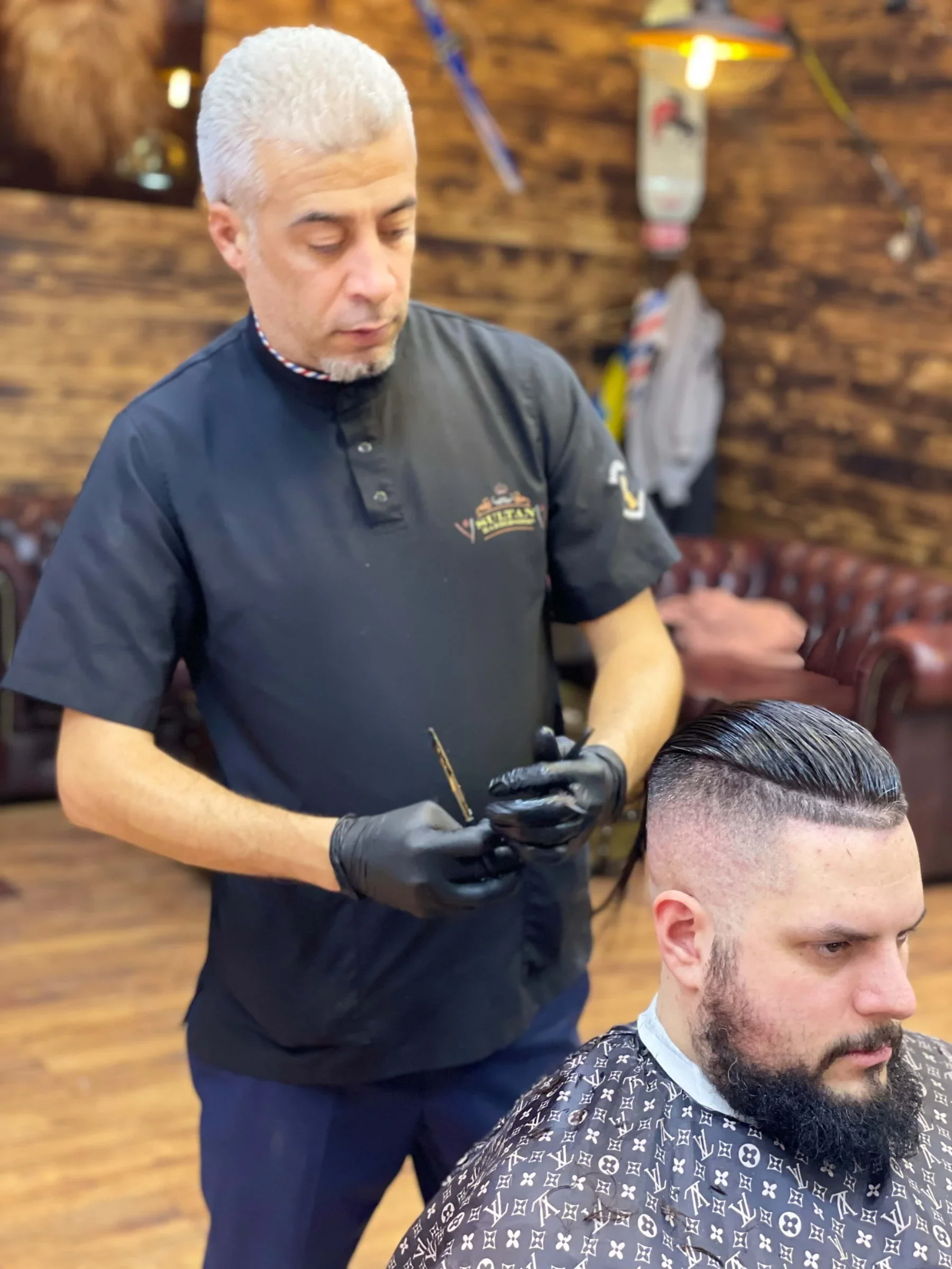 Barber styling a man's hair in a barber shop with wood-paneled walls.