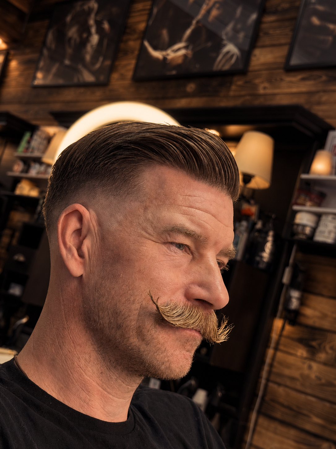 A man with a slicked-back hairstyle and a curled mustache in a barbershop.