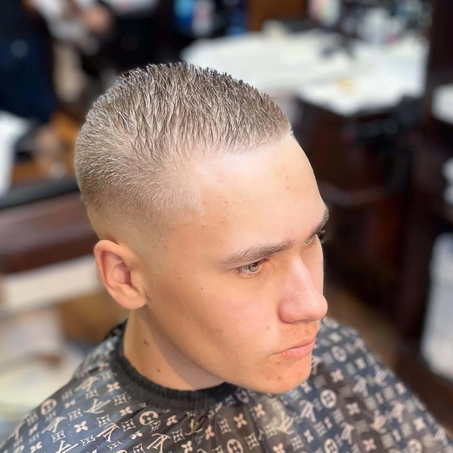 Young man with a freshly cut fade hairstyle, sitting in a barbershop chair, looking to the side.
