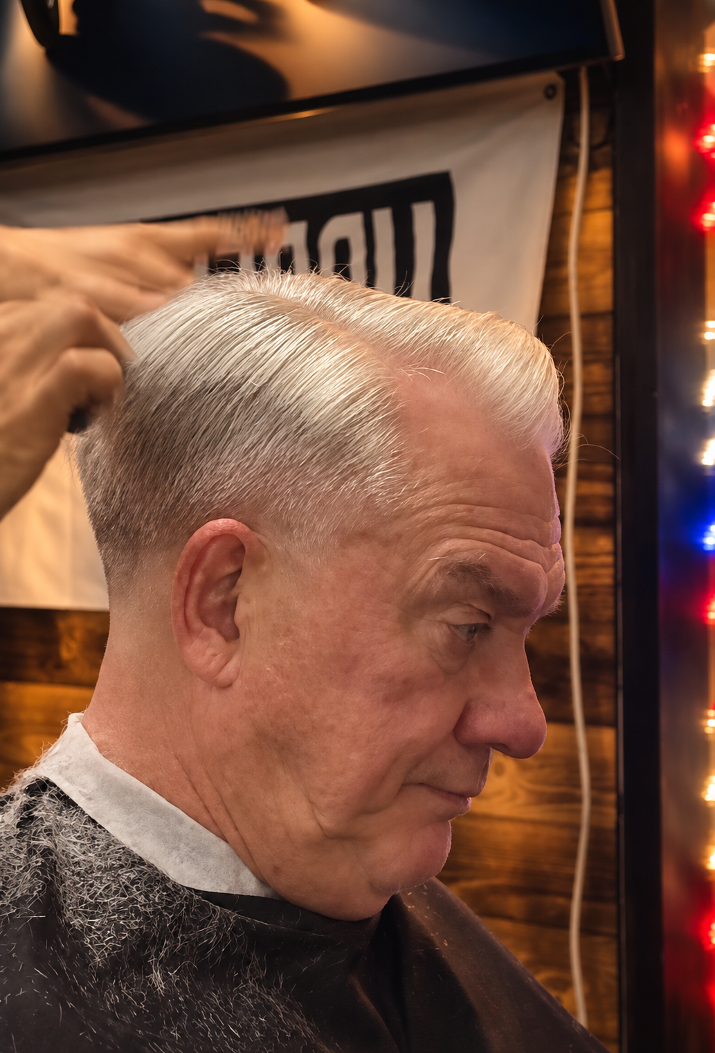 An older man getting a slicked back, platinum blonde hairstyle at a barbershop.