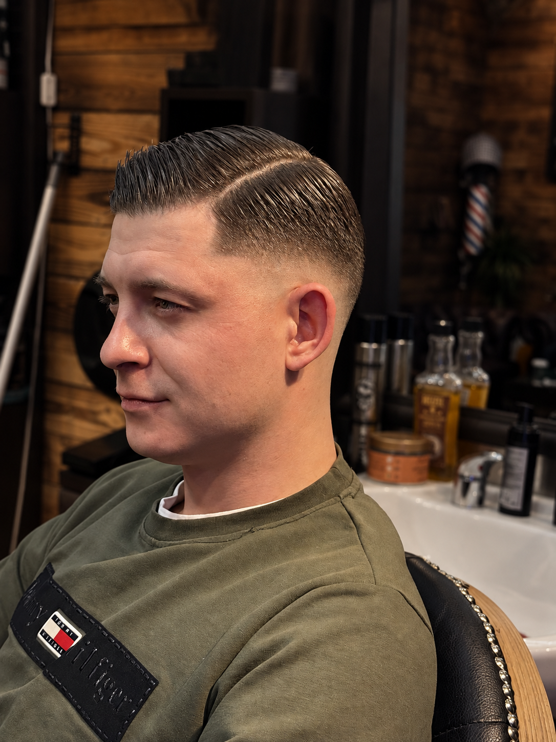 A man with a freshly styled slicked-back haircut sitting in a barbershop chair.