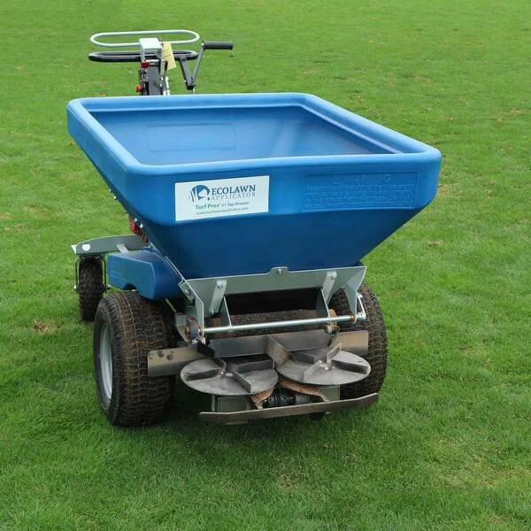 Blue turf fertilizing cart with wheels and a handle, on a grassy field.