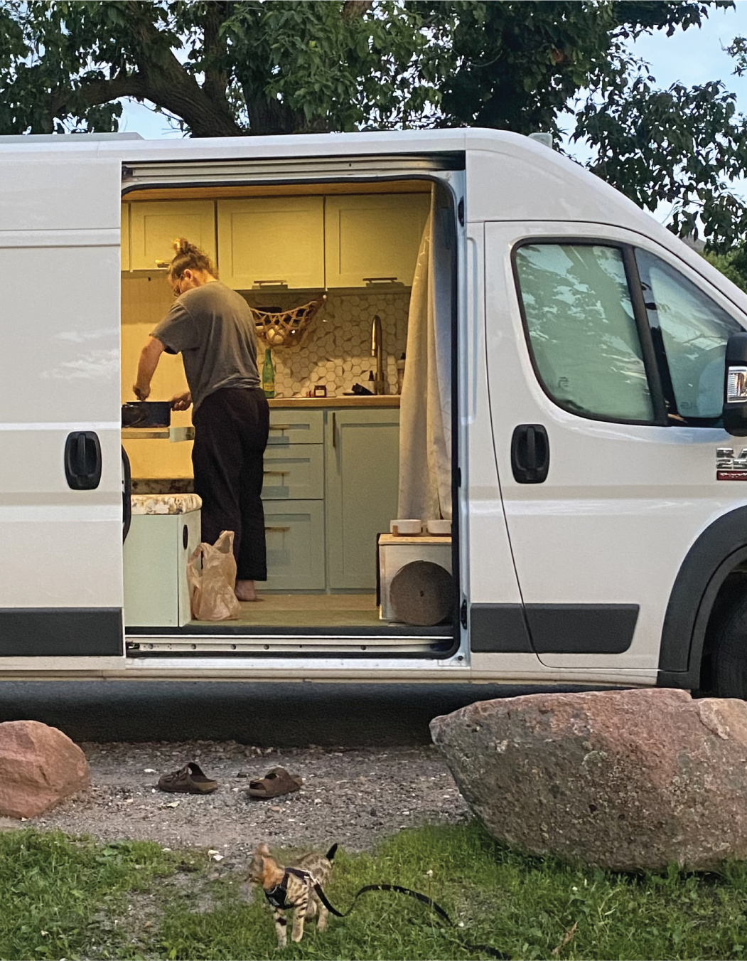cooking inside a converted camper van equipped with a Basecamp Collective modular kitchen kit, showcasing compact car camping design and functionality.