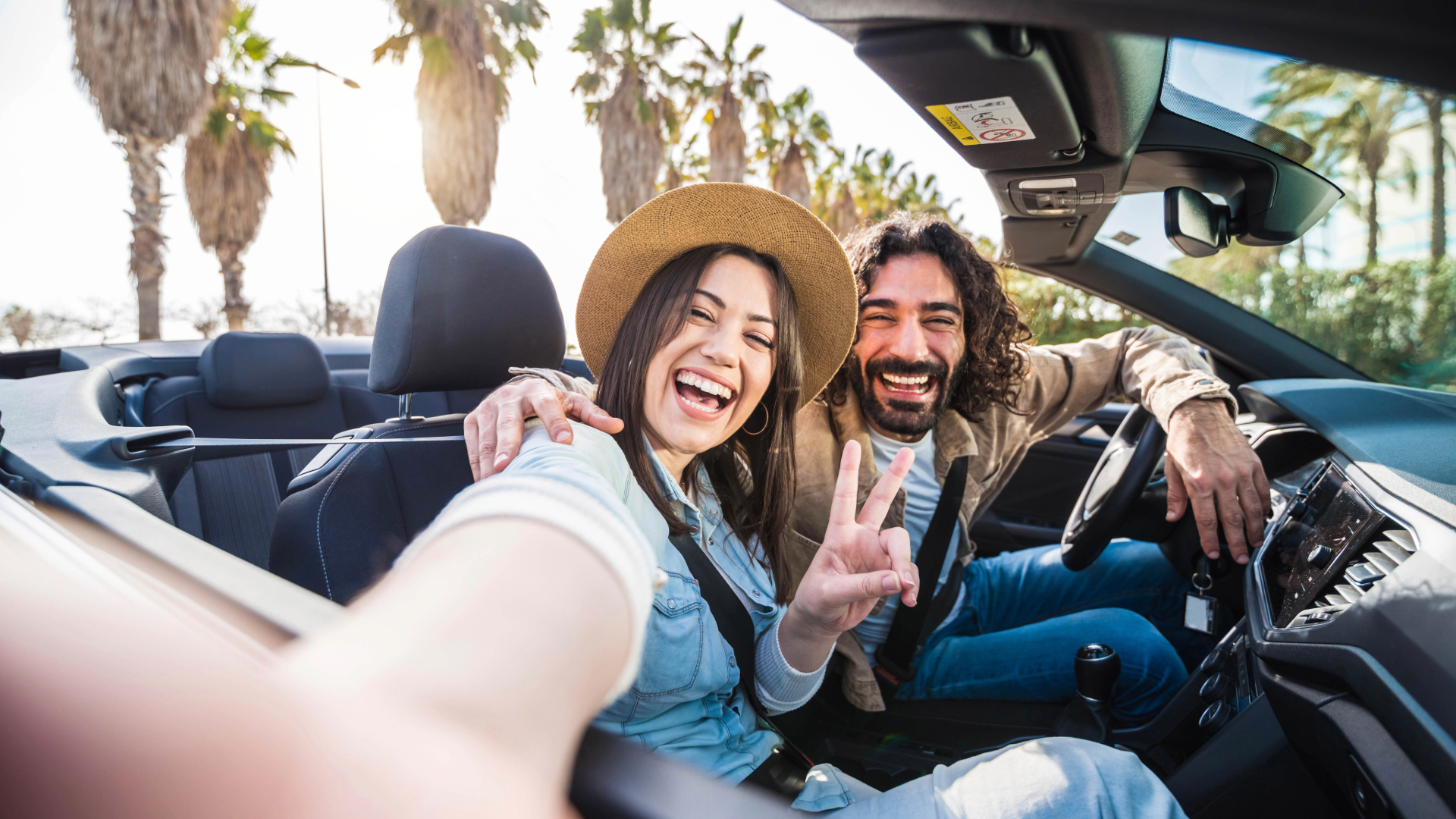 couple in convertible car giving the peace sign with palm trees in background