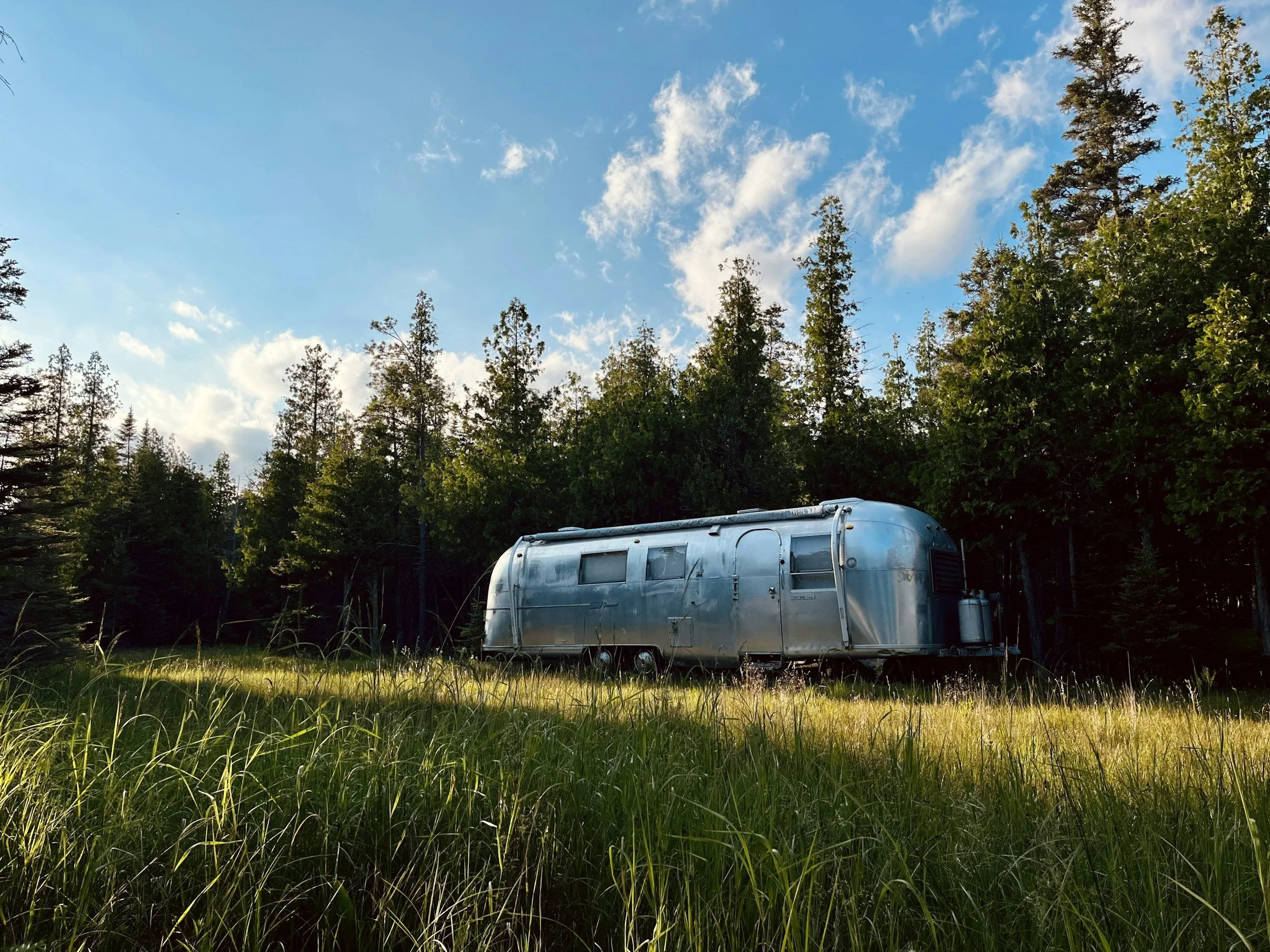 silver airstream travel trailer parked in wooded area next to field