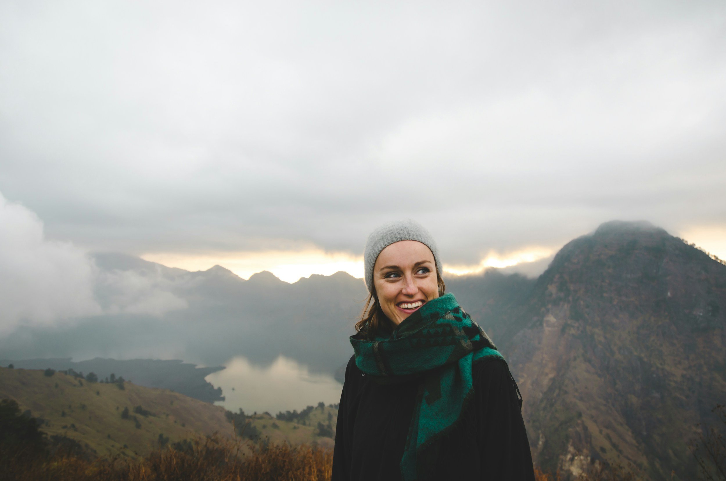 smiling lady outdoors on mountainside with a wool hat and scarf near a lake