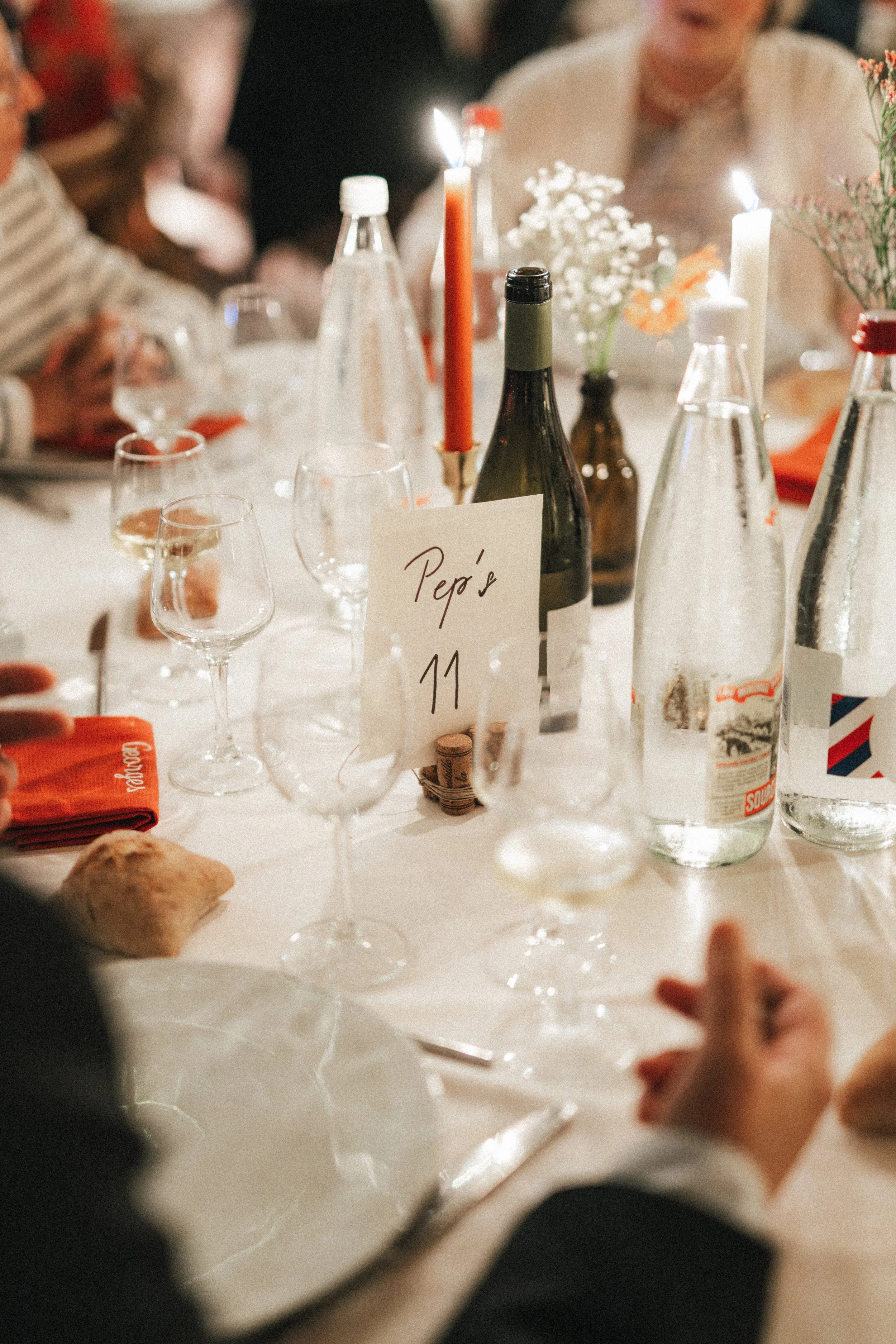 Table de dîner avec des verres à vin, une bouteille de vin, des bouteilles d'eau, des bougies allumées, des fleurs, et une carte avec l'inscription "Repas 11".