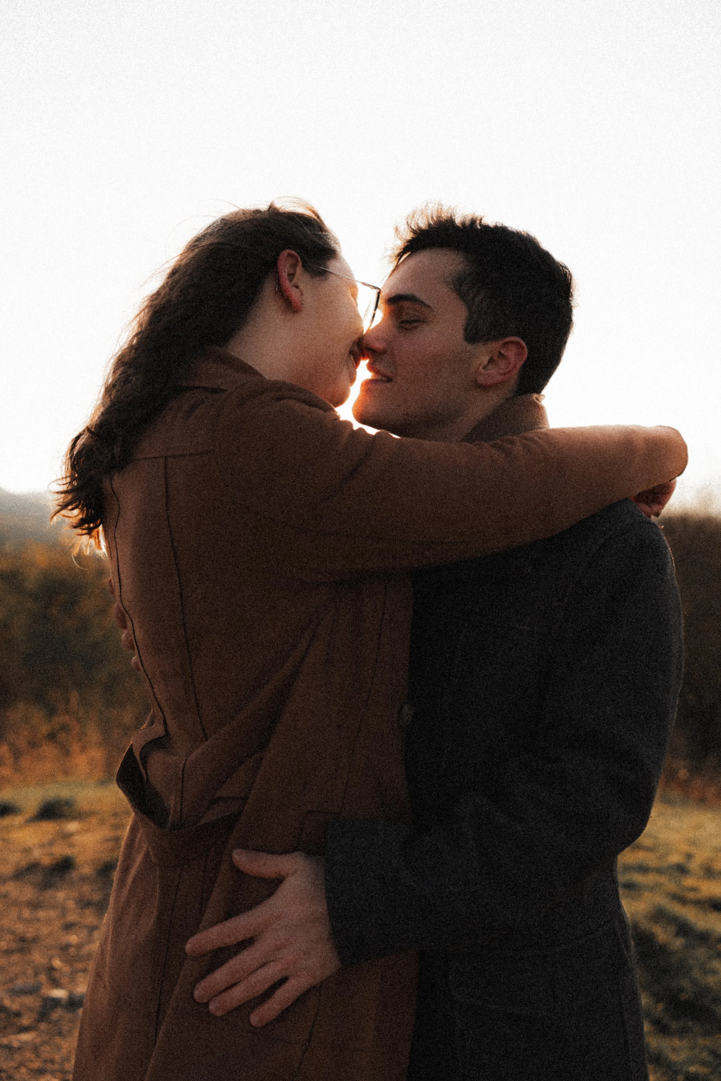 Un couple qui s'enlace et se sourit tendrement lors d'un coucher de soleil en plein air.