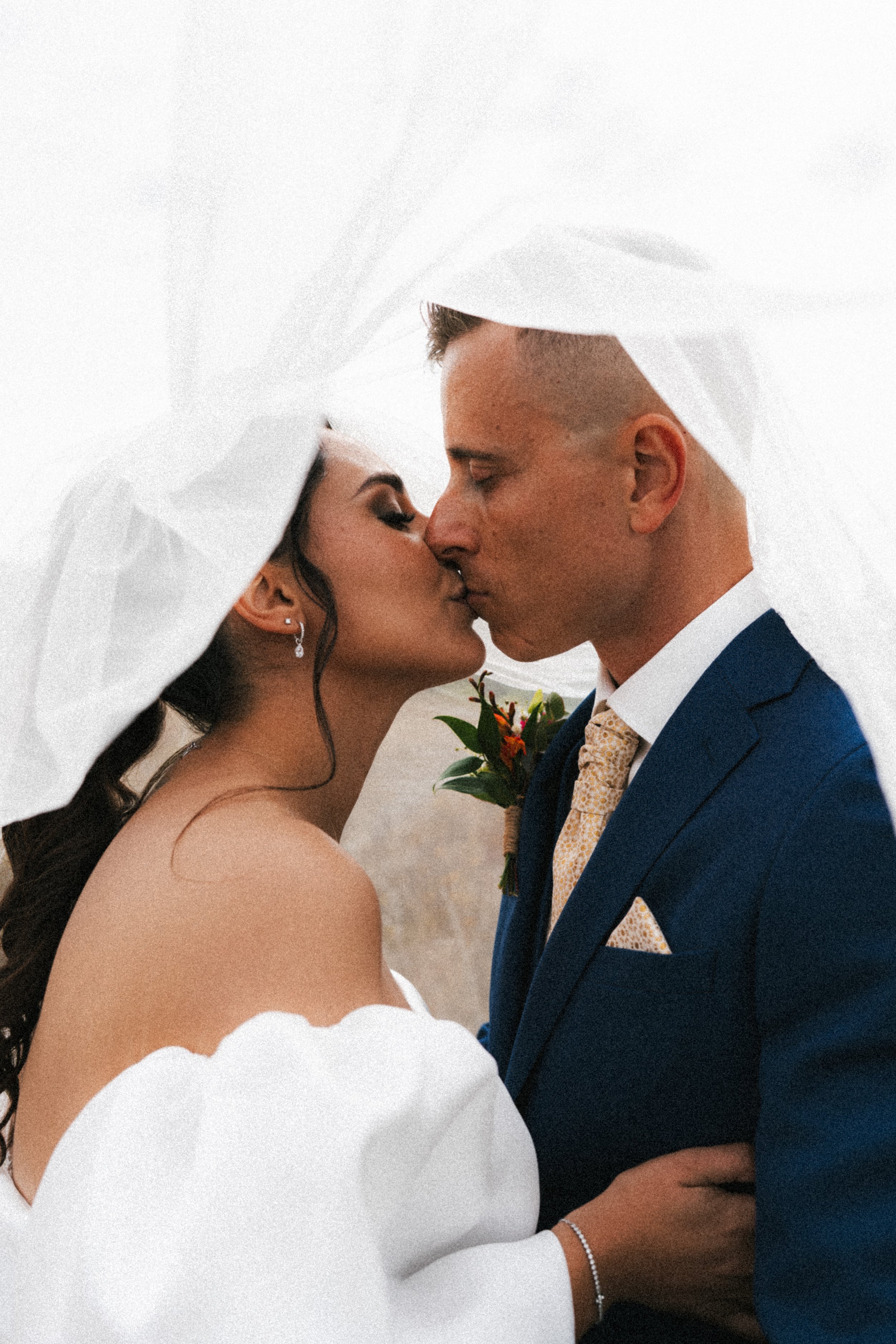 Un couple marié s'embrassant sous un drap blanc lors de leur mariage.