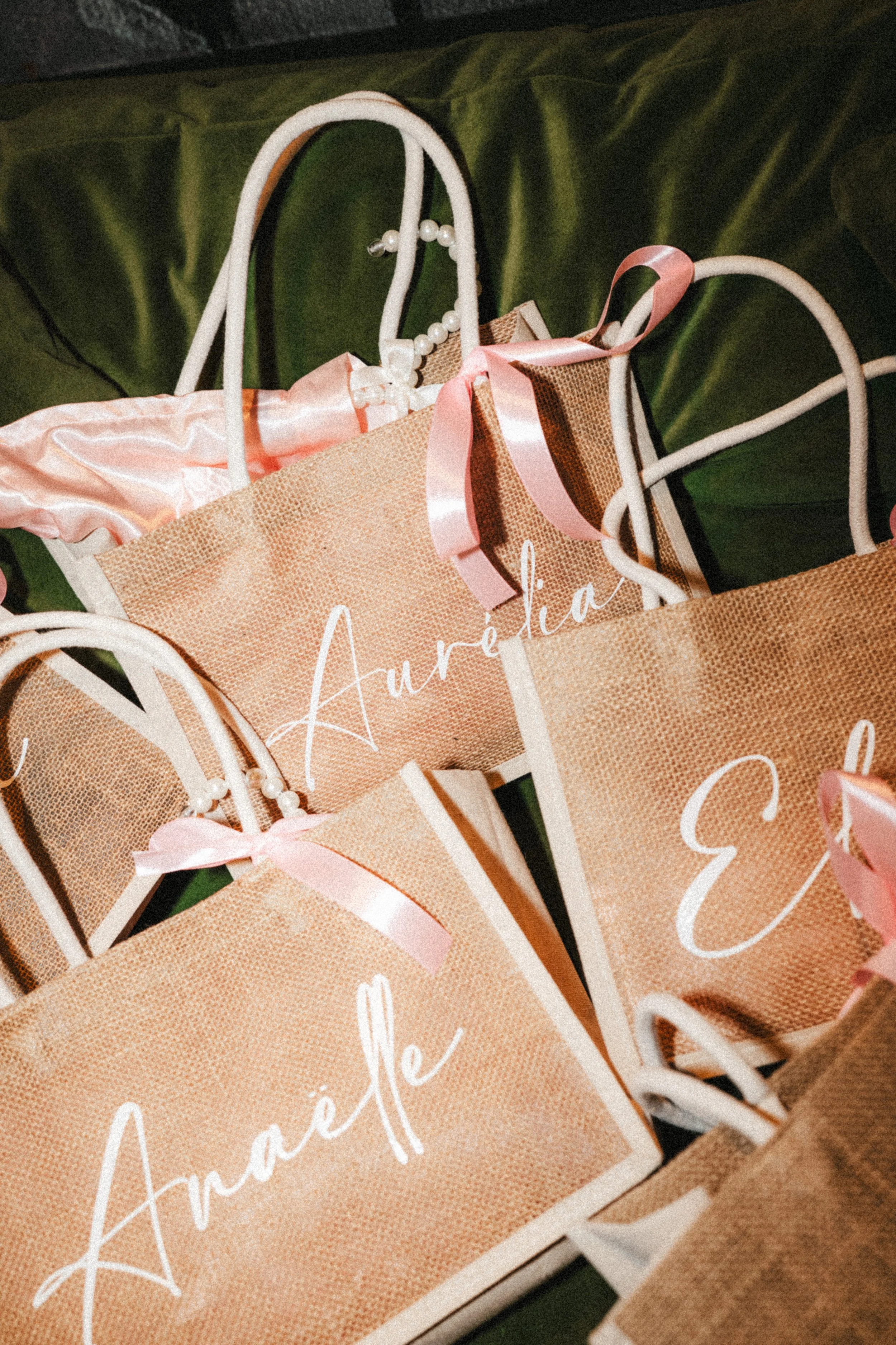Gobelets en papier personnalisés avec le nom 'Aurélia', décorés avec des rubans roses, disposés sur un fond vert. 