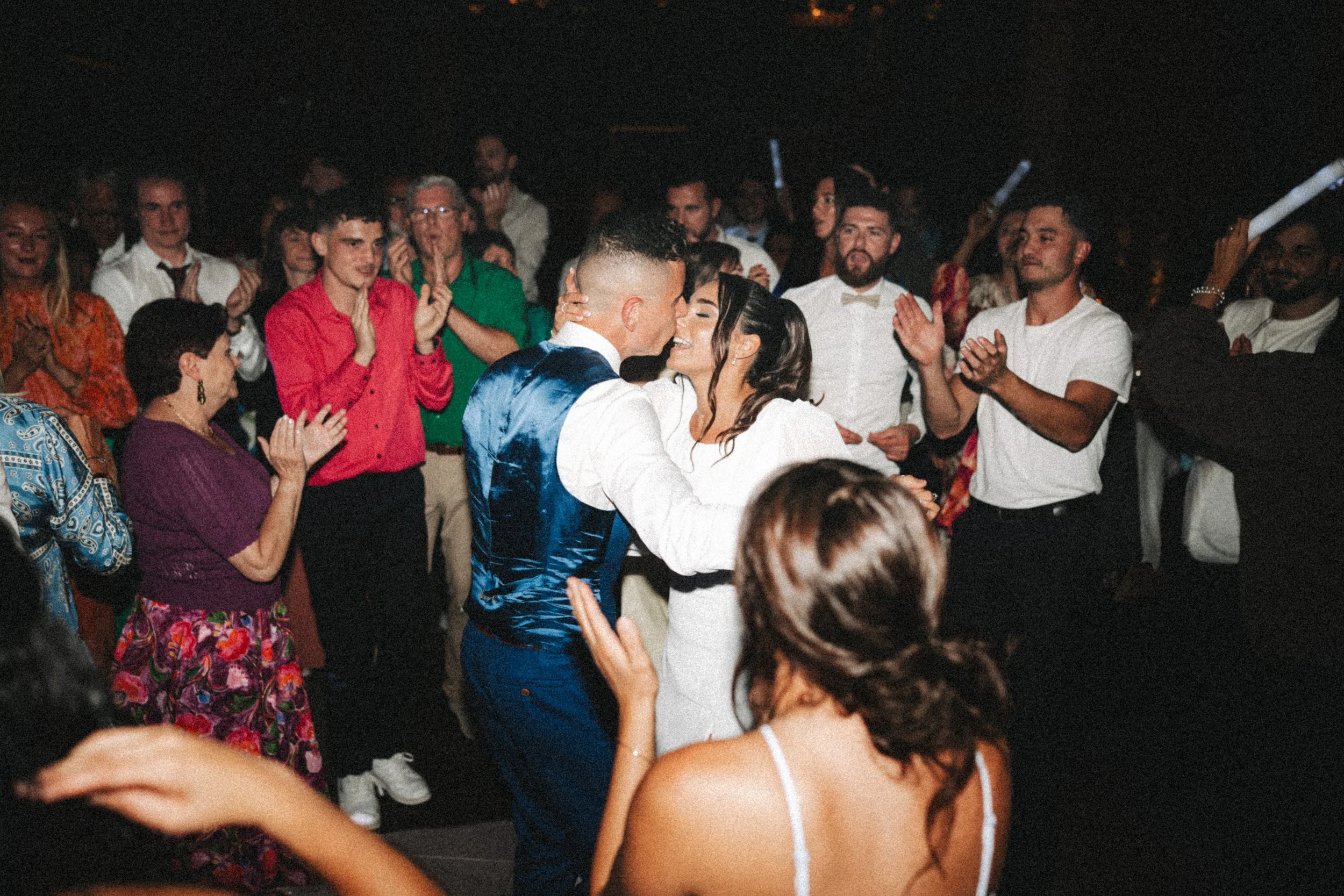 Un couple en train de danser lors d'une célébration entourée de personnes qui applaudissent, dans une ambiance festive.