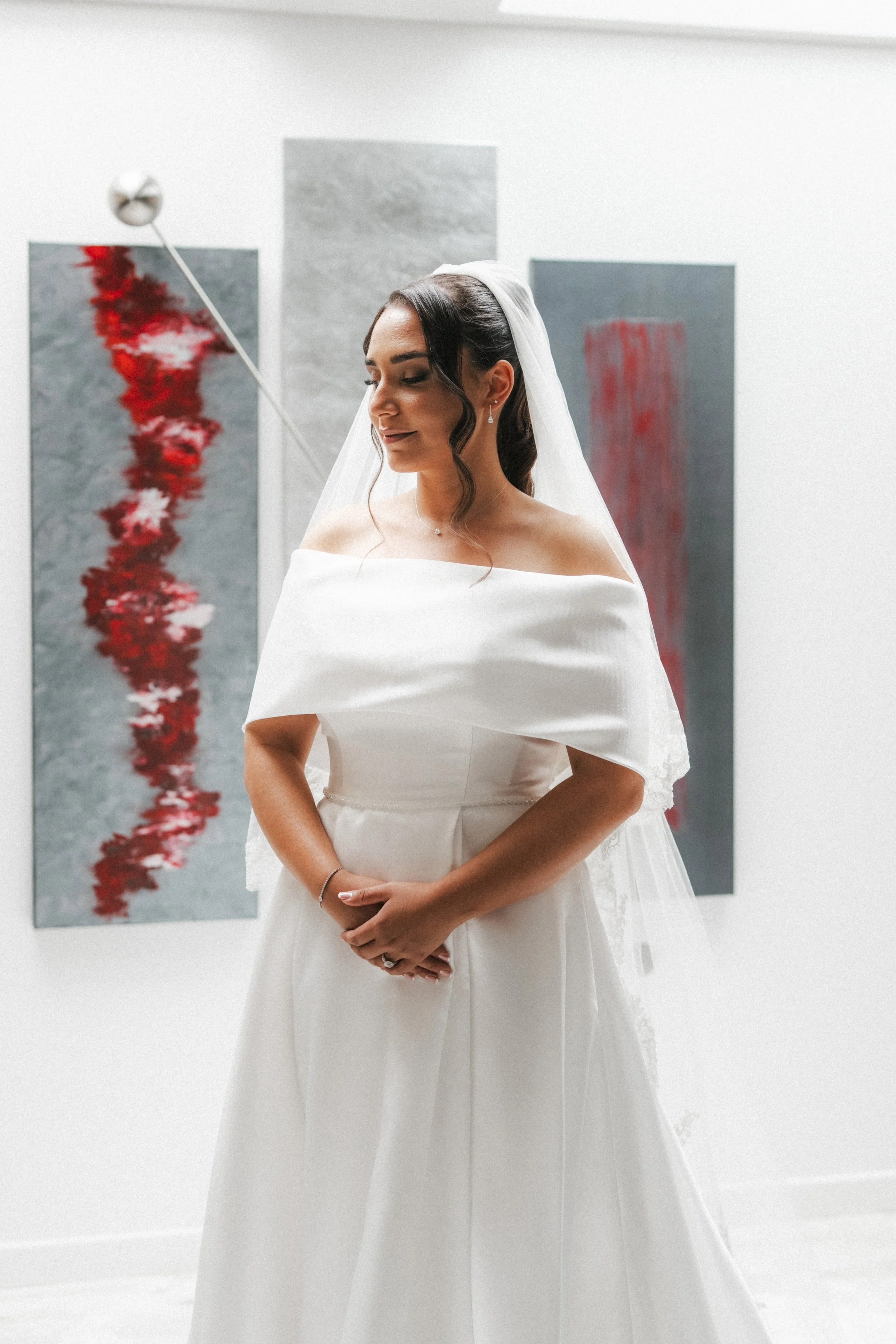 Une jeune femme en robe de mariée blanche, portant un voile, se trouve devant des œuvres d'art abstraites dans une galerie.