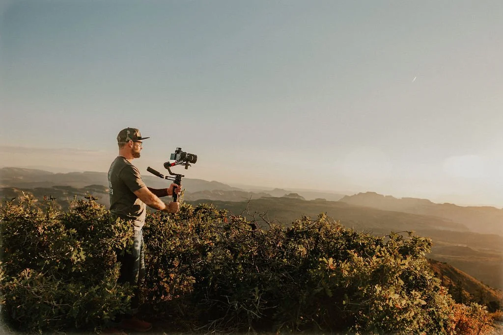 A man with a camera stabilizer filming a landscape during sunset