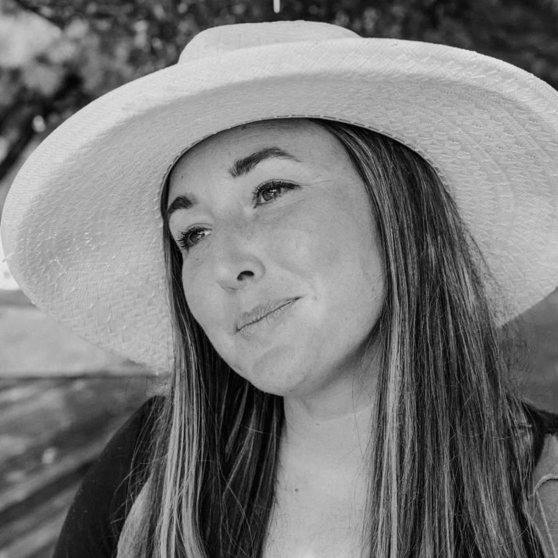 A woman wearing a large sun hat and smiling softly outdoors.