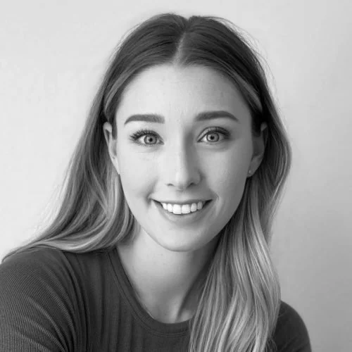 A young woman with long hair, one eye winking, smiling, wearing a dark top, in a black-and-white photo.