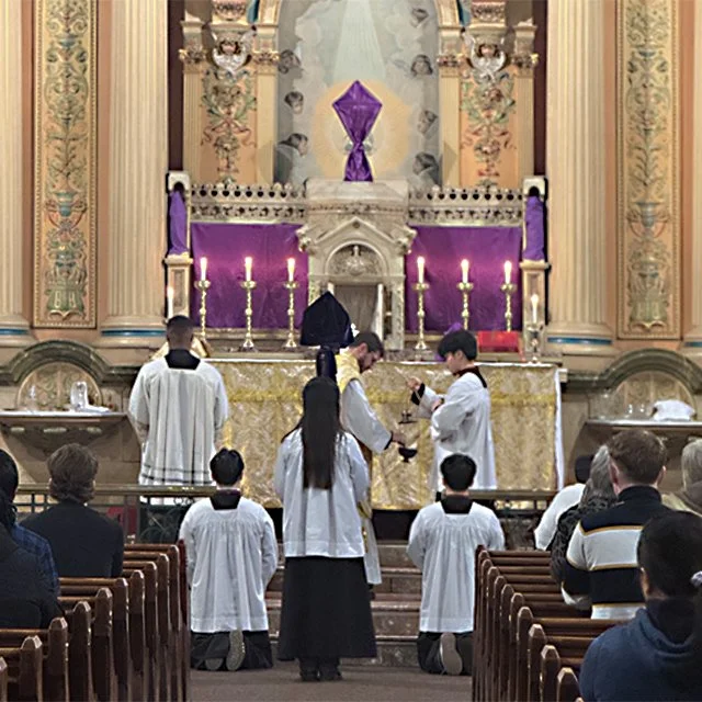 Children in white robes participating in a religious ceremony at a church altar with candles and purple decorations.