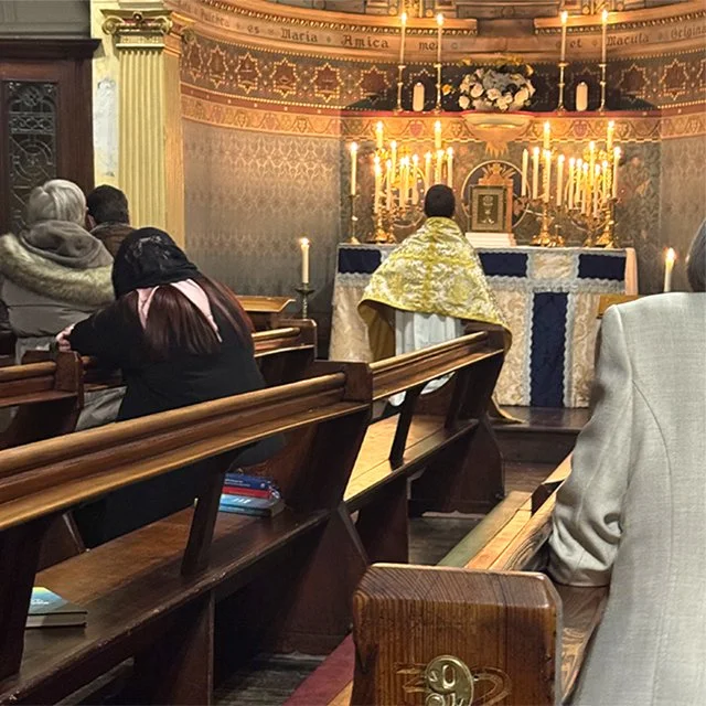 People praying in a church with an altar decorated with candles and flowers.