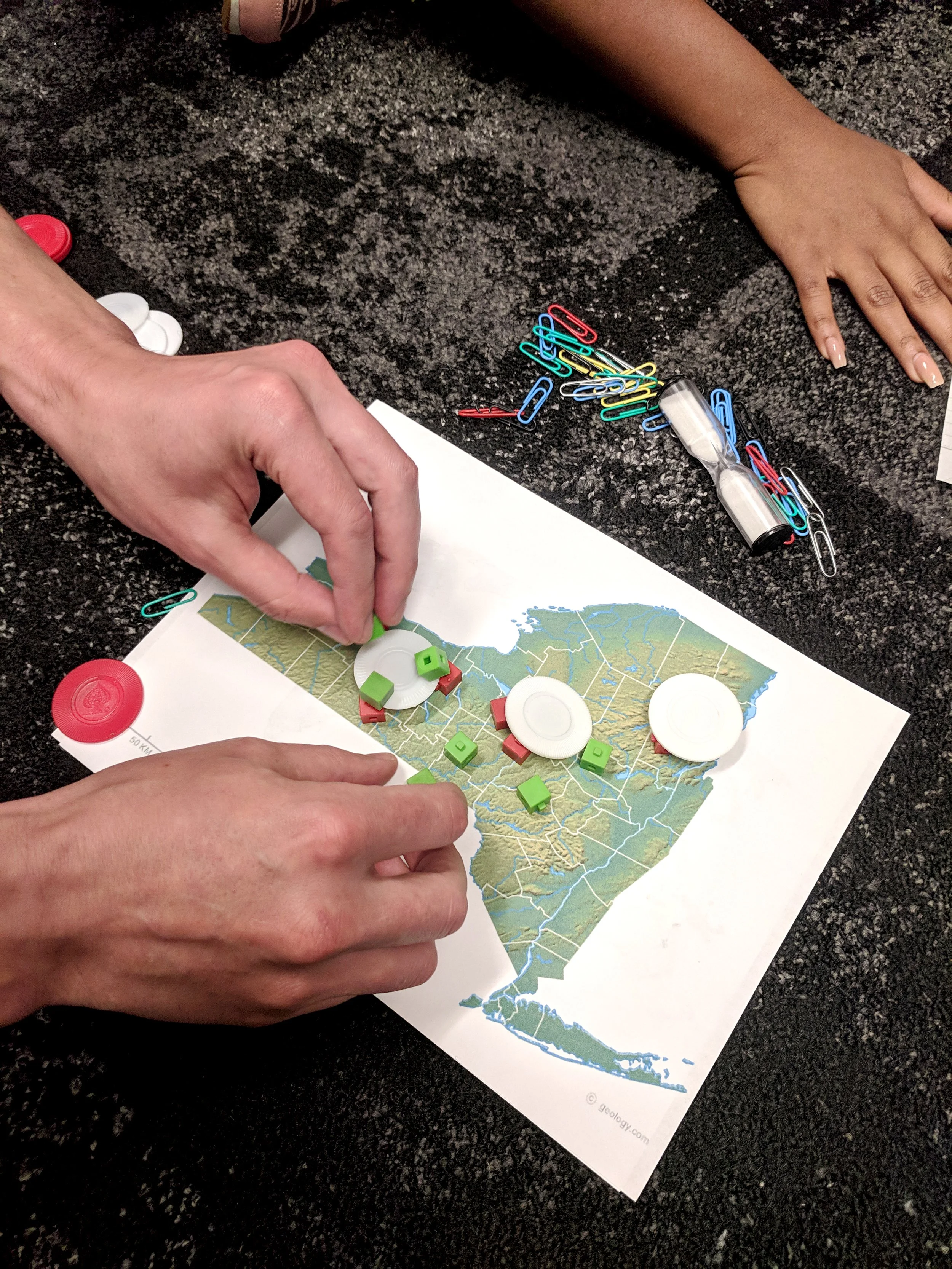 Two hands moving game pieces on a map of NY State