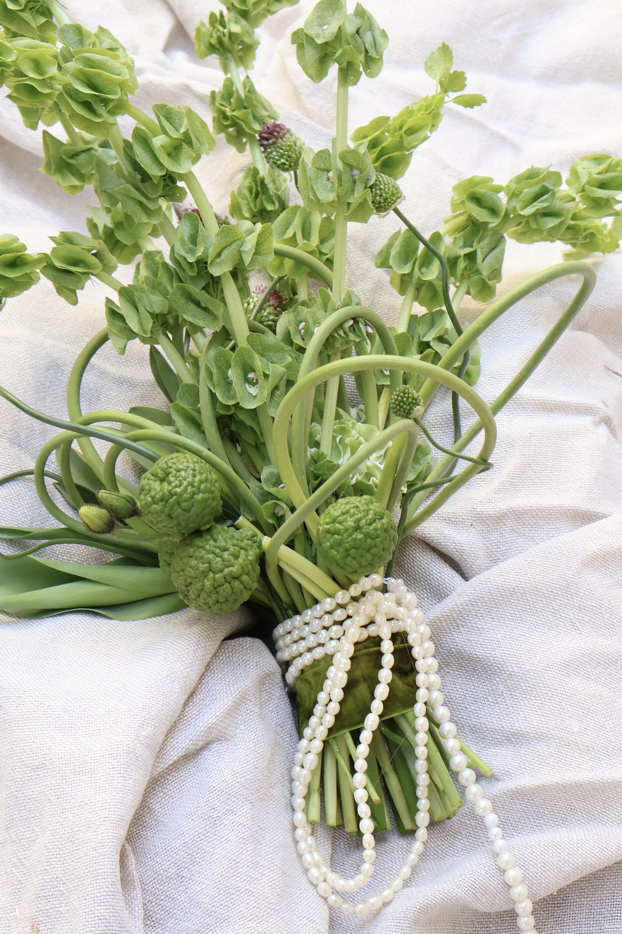A modern bouquet of green florals adorned with white pearl necklaces.