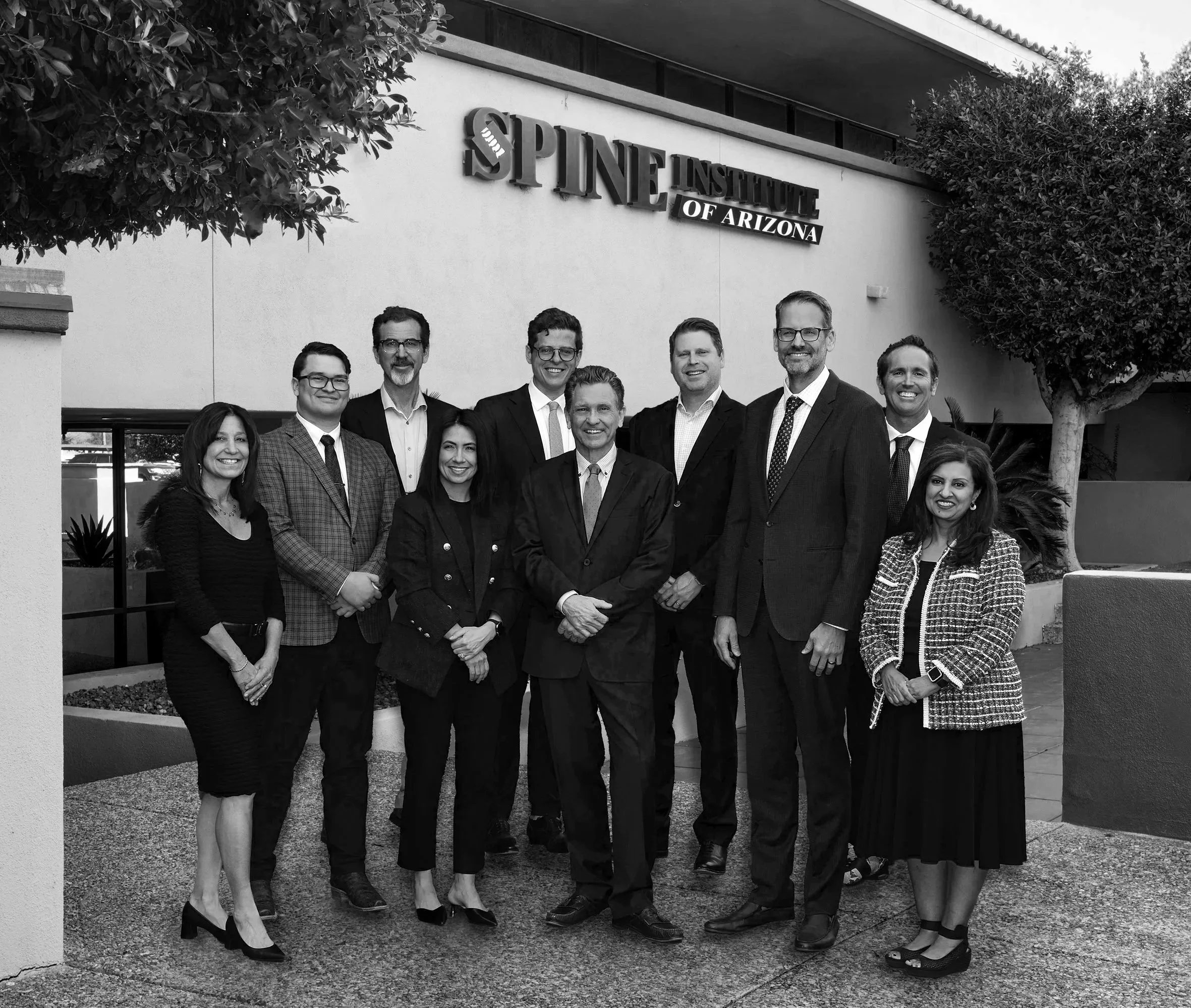 A group of eleven professionally dressed people standing outside a building with a sign reading 'Spine Institute of Arizona'.