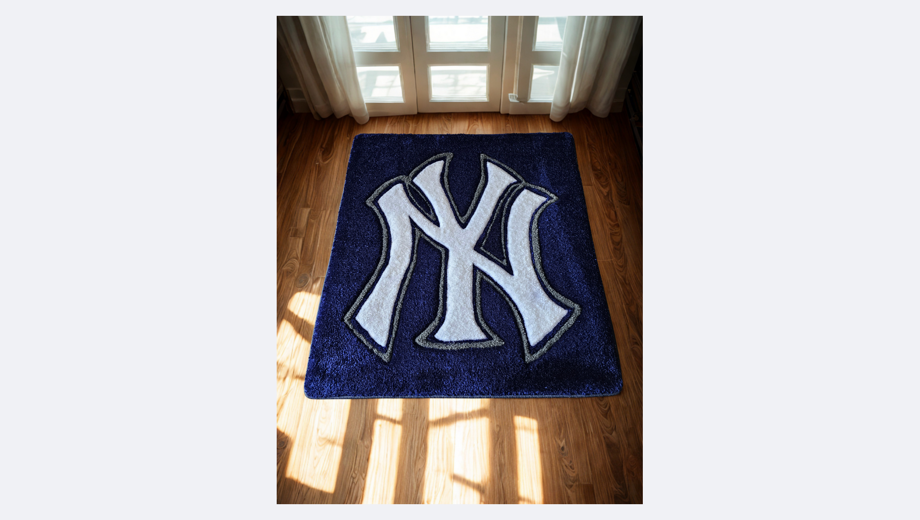A blue rug with the New York Yankees logo in white and black, placed on a wooden floor in front of glass doors with white curtains.
