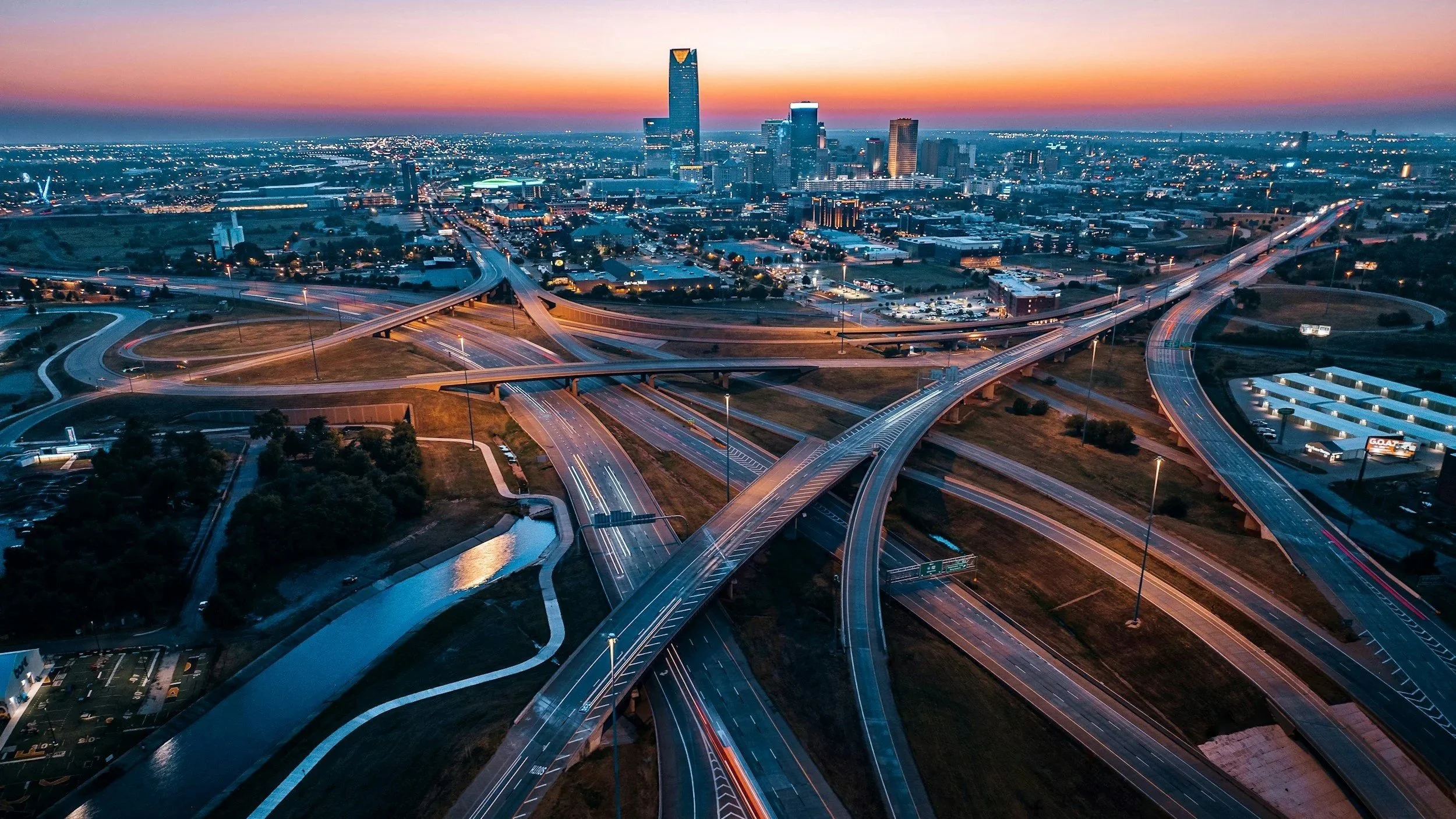 Aerial view of a city skyline at sunset with multiple highway ramps and roads in the foreground.