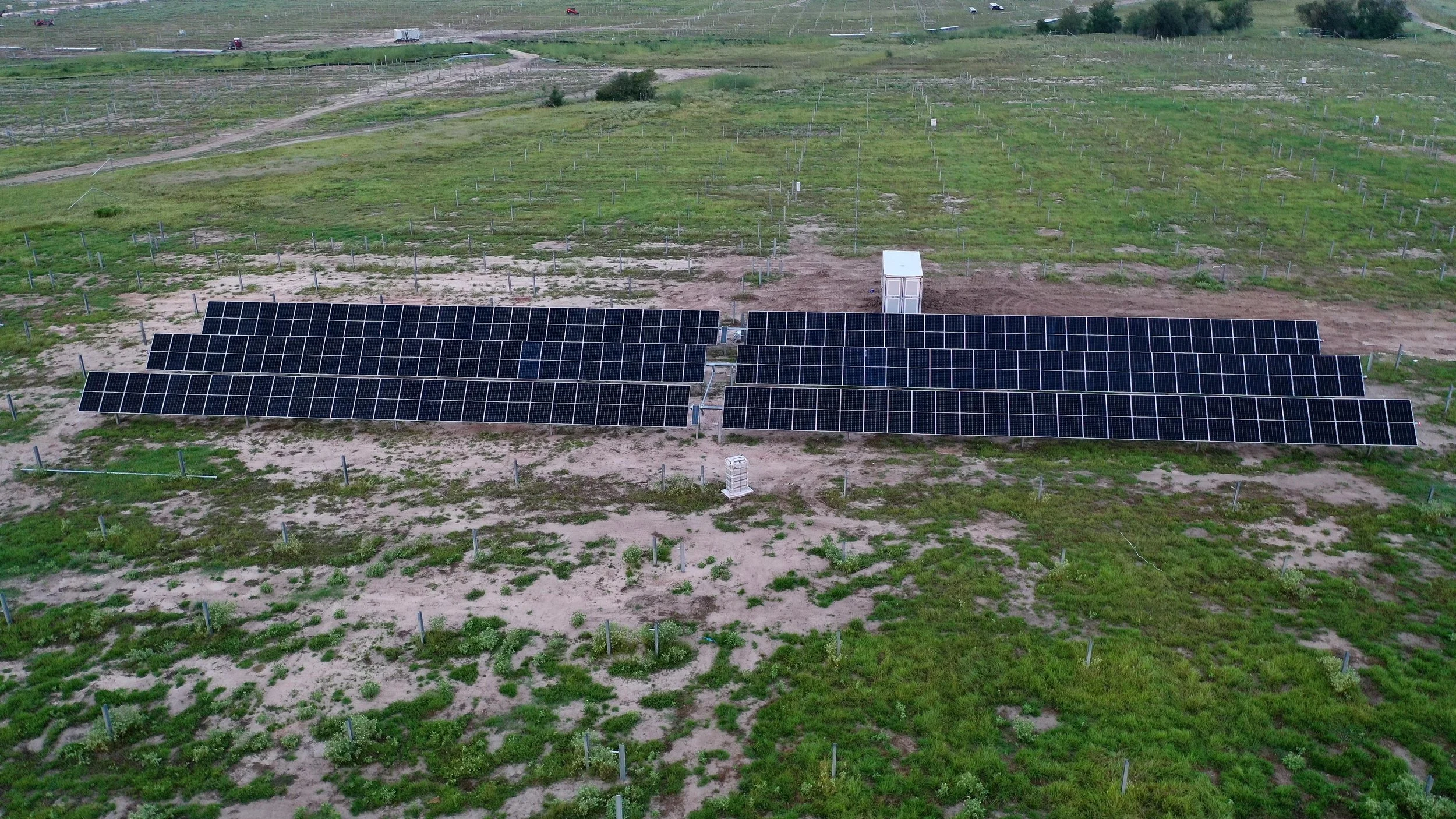 Aerial view of a solar farm with rows of solar panels installed on a grassy and sandy field.