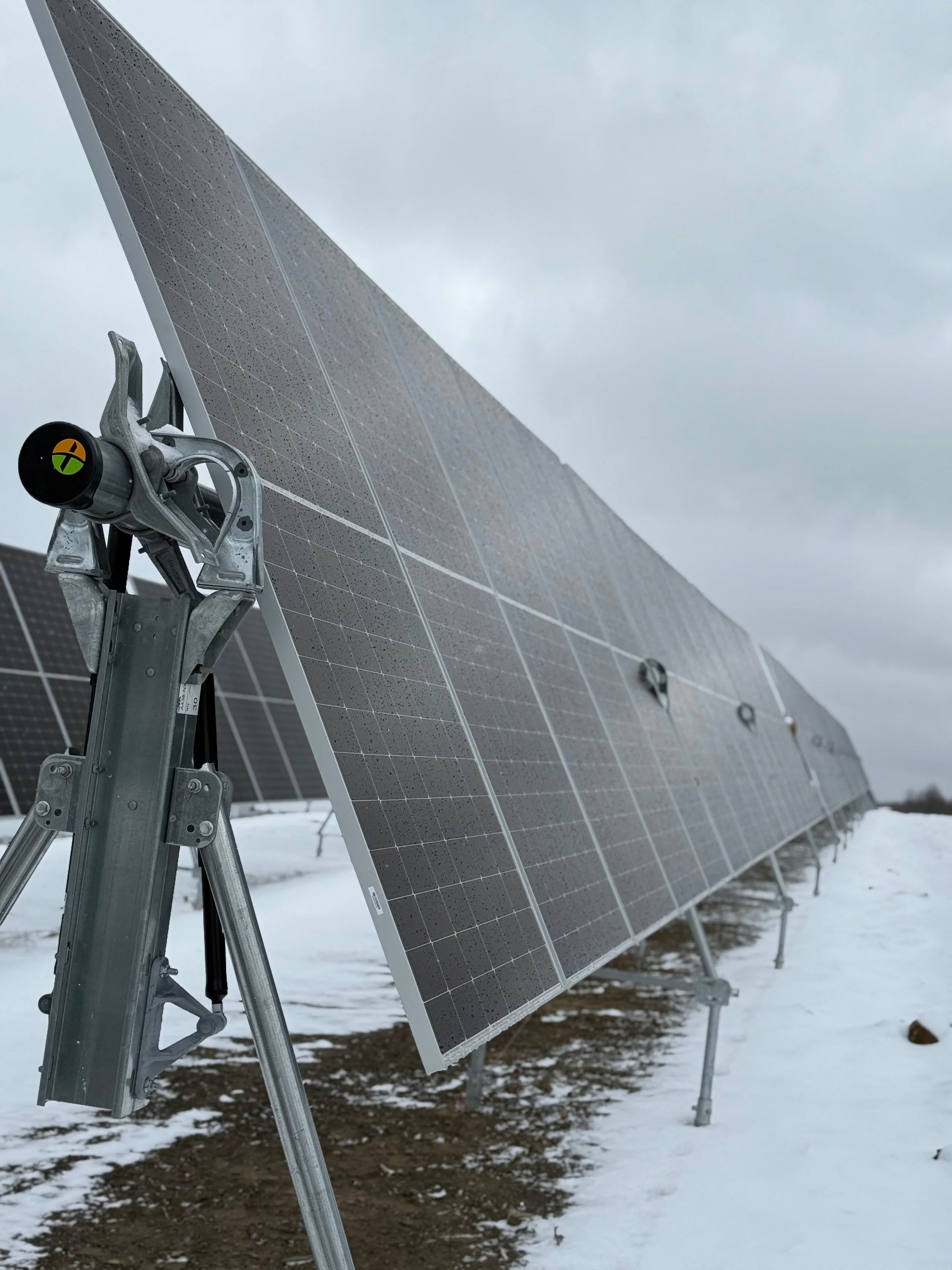 Solar panels installed outdoors on snowy terrain, with an overcast sky.
