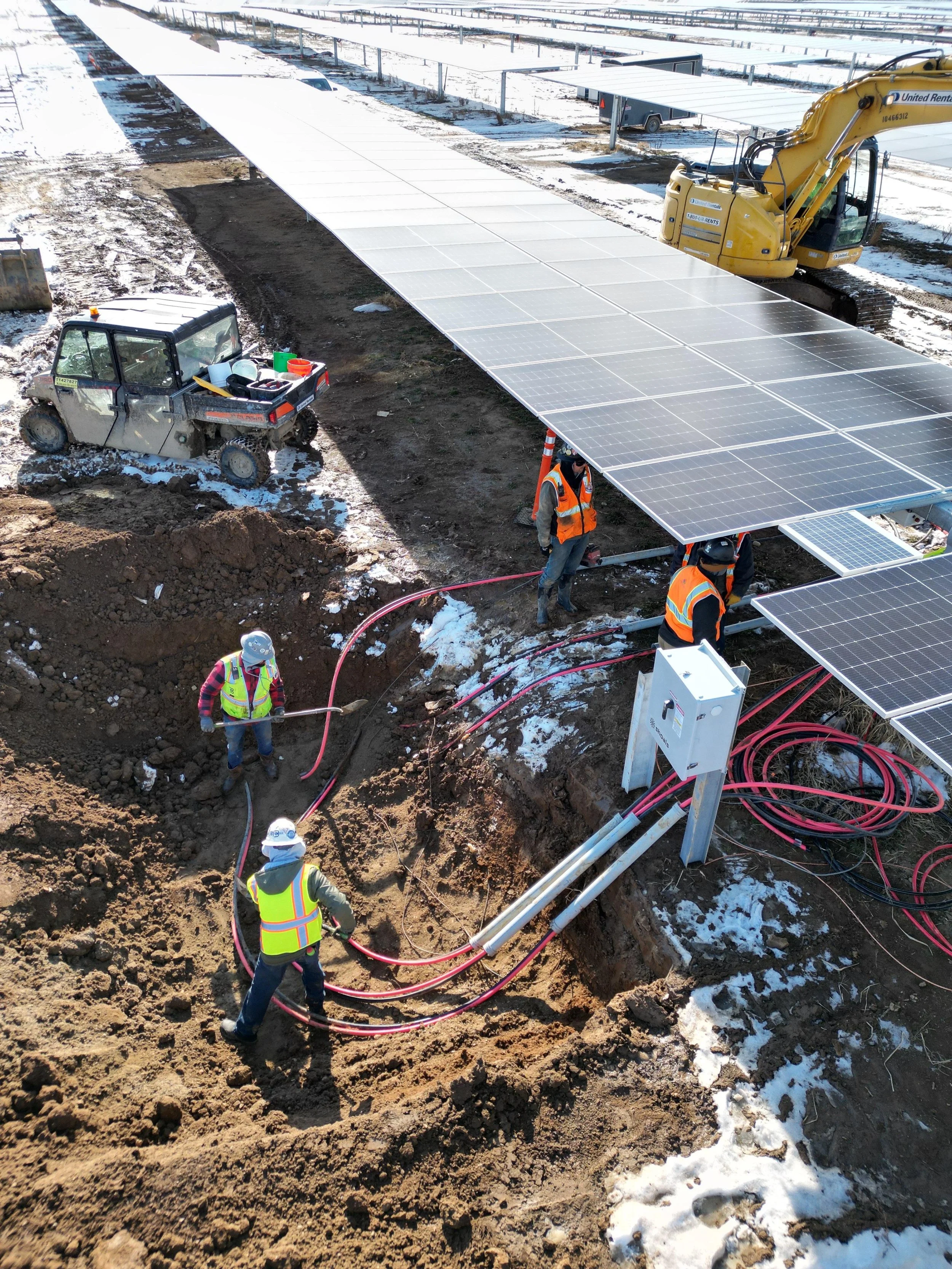 Construction workers installing solar panels on a solar farm in snowy weather.